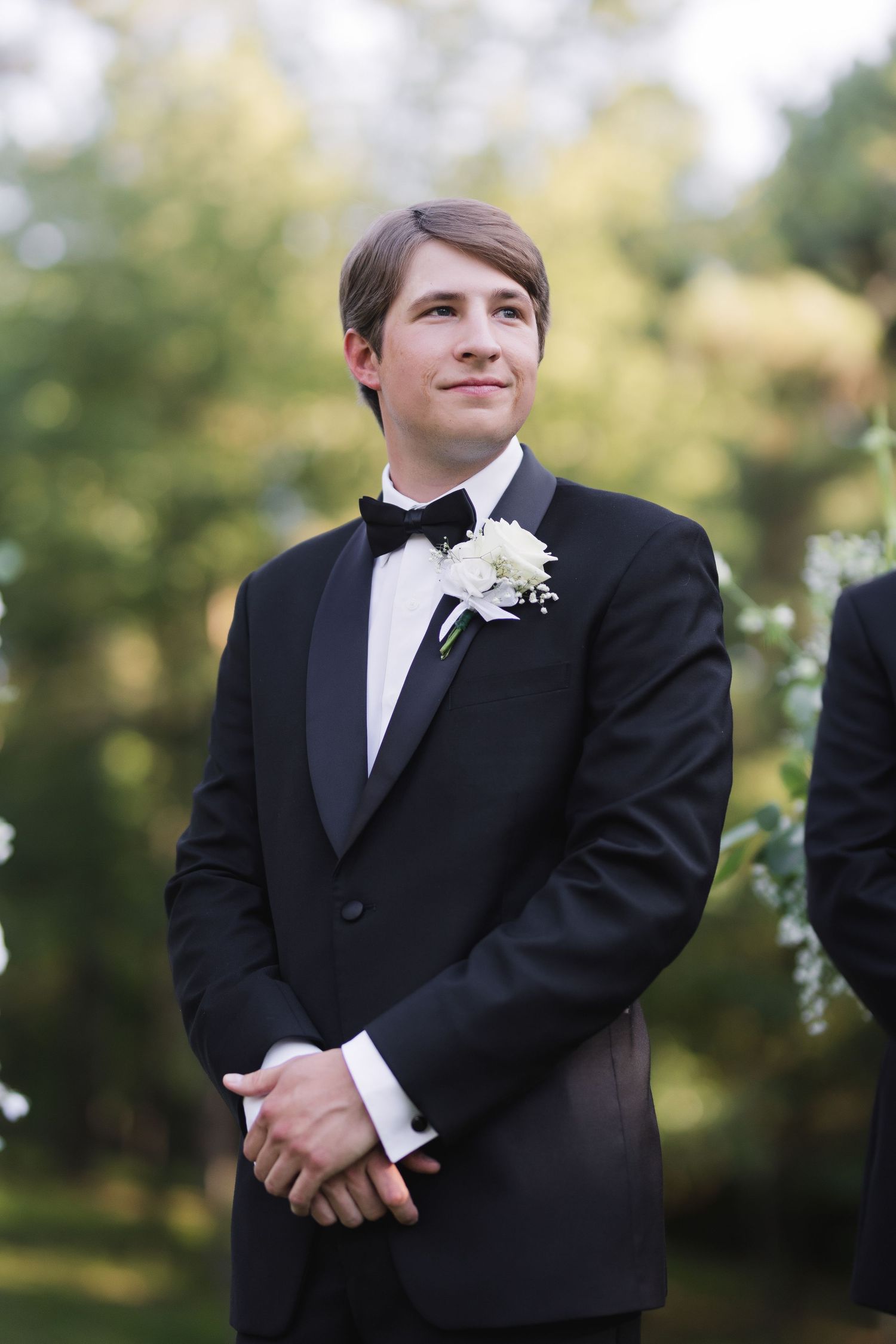 Formal portrait of groom in classic black tuxedo with white boutonniere.