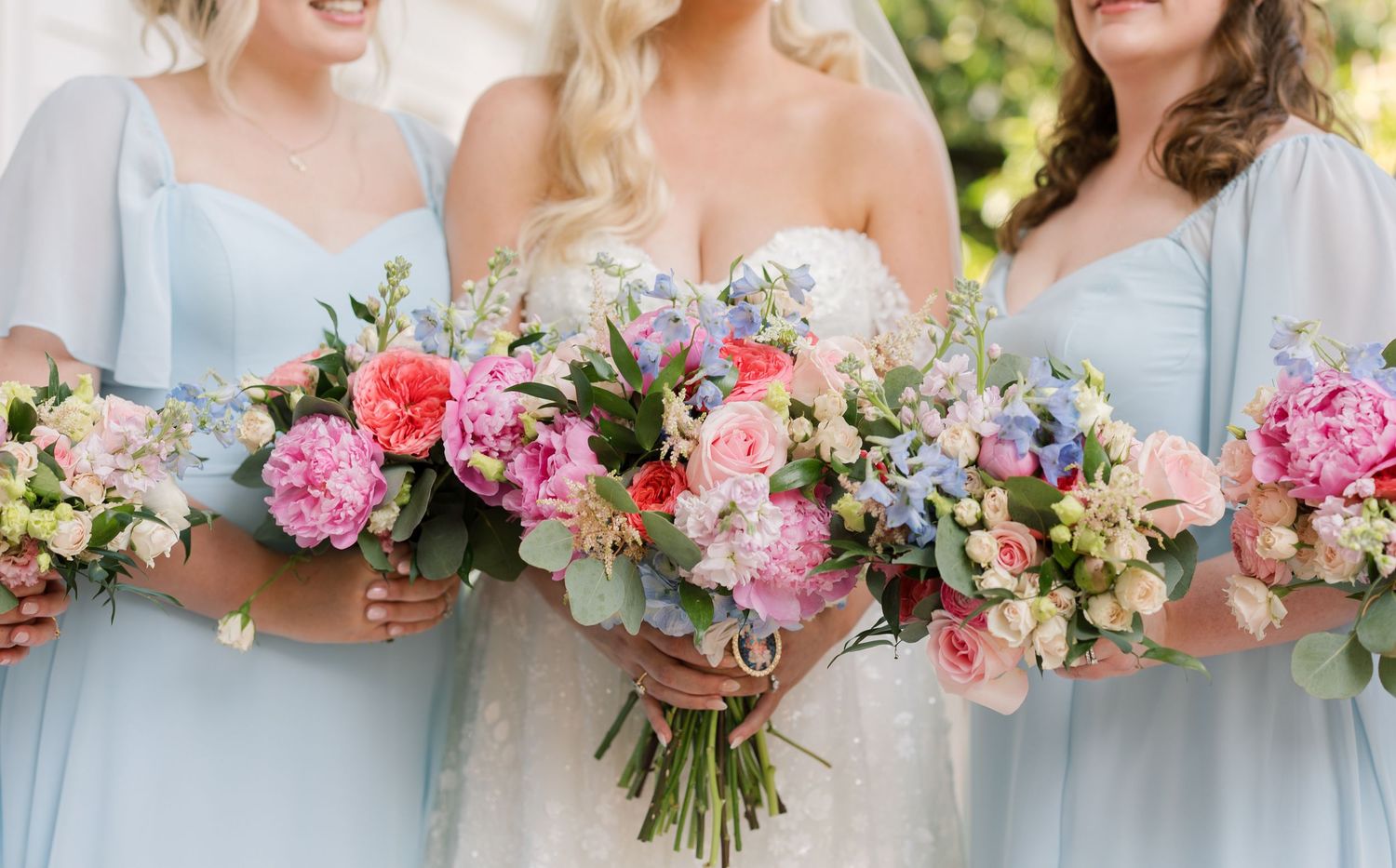 Bridesmaids in light blue dresses hold vibrant pink and purple flower bouquets.
