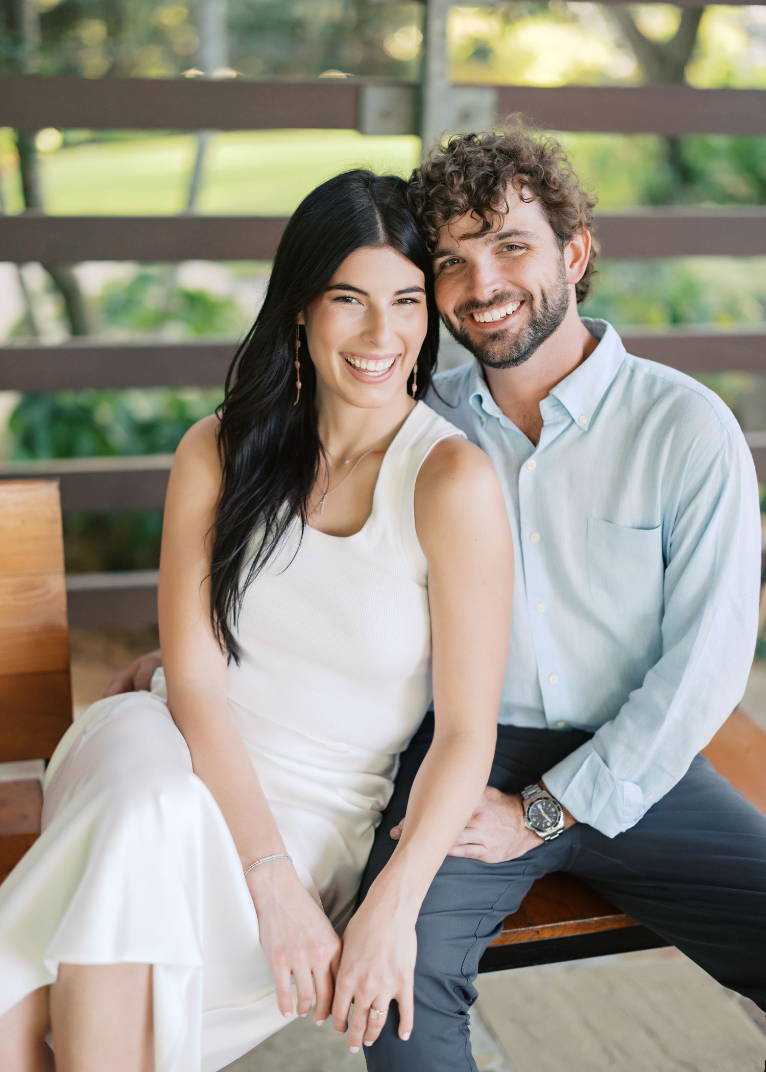 Couple shares intimate moments while sitting on wooden bench outdoors.