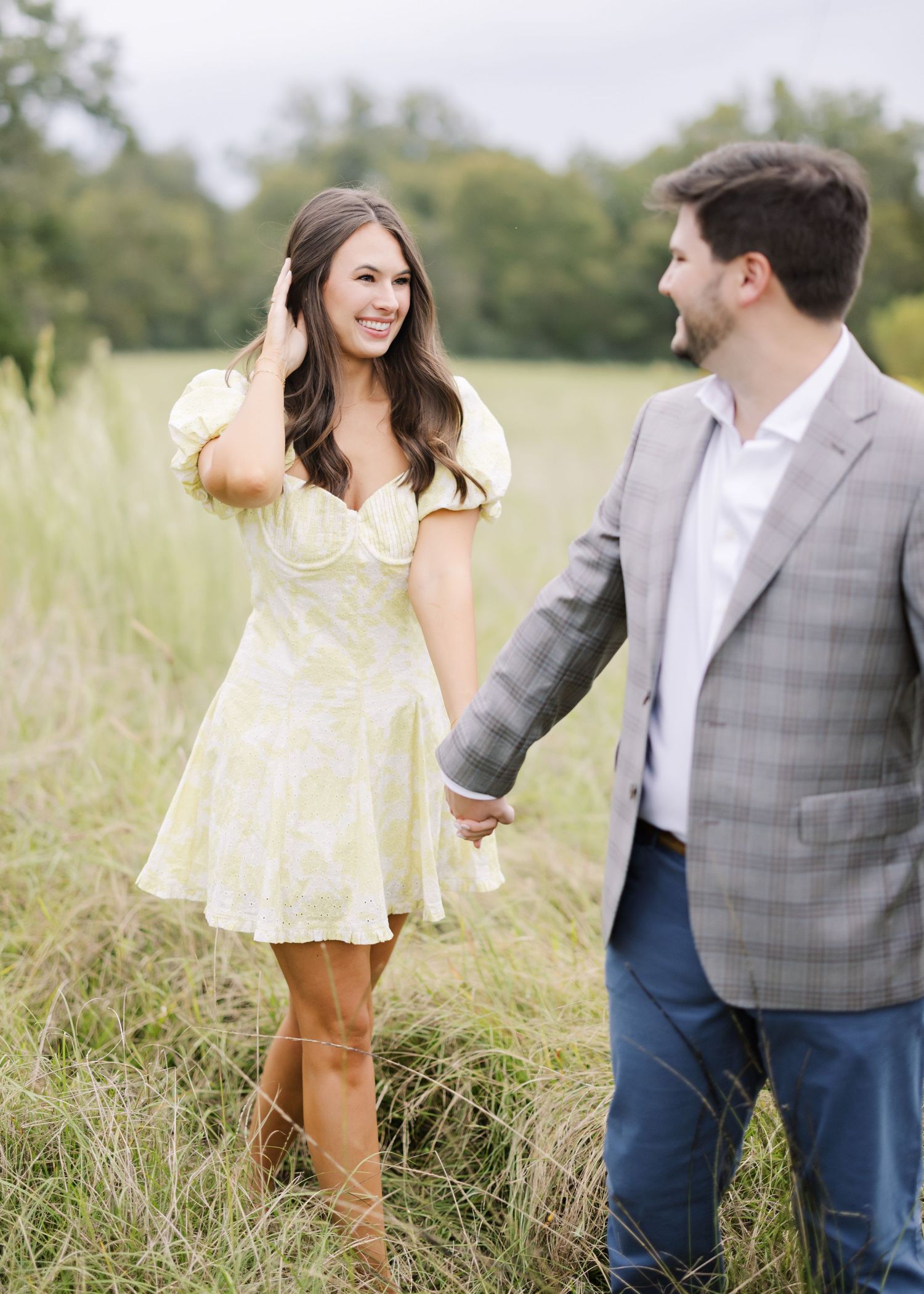 A couple walking together in a sunny meadow with tall grass.