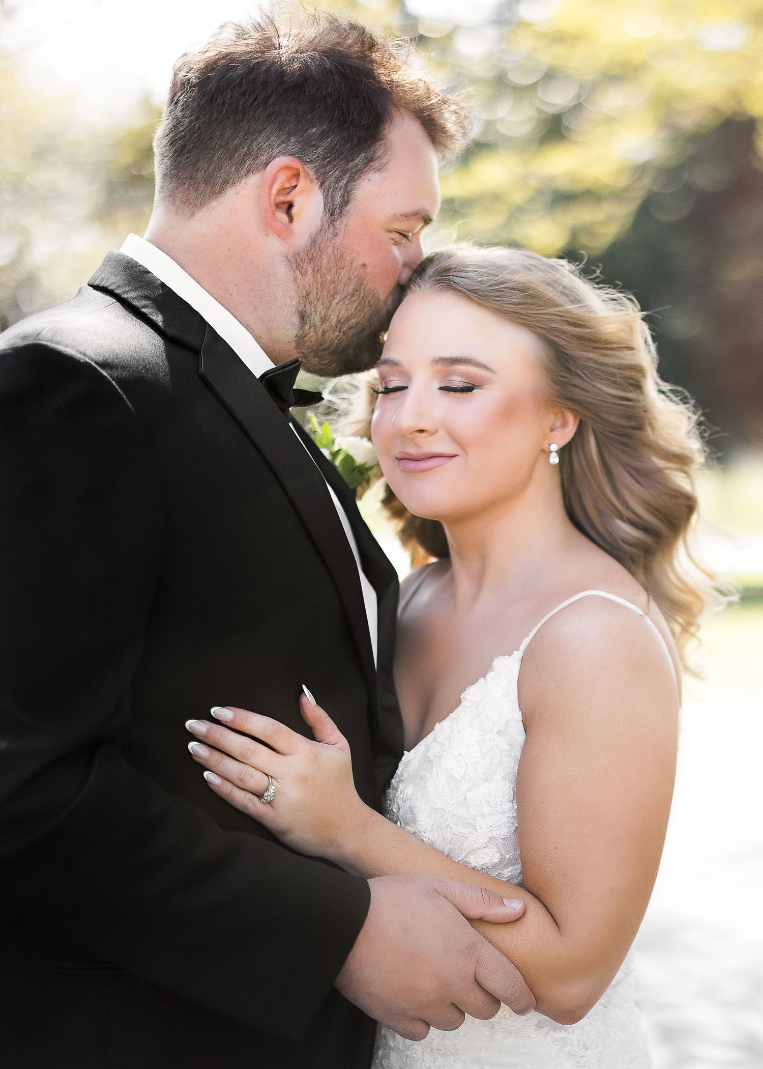 Wedding couple embraces in golden sunlight with bride in white lace gown.