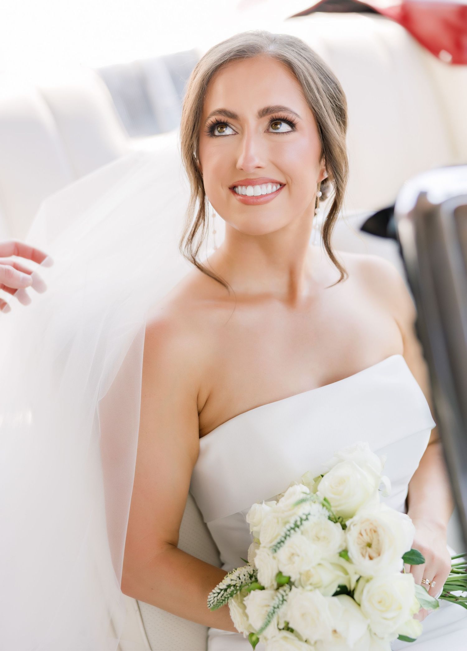 A bride in an elegant white strapless gown holds a classic white and cream bouquet during her wedding celebration.