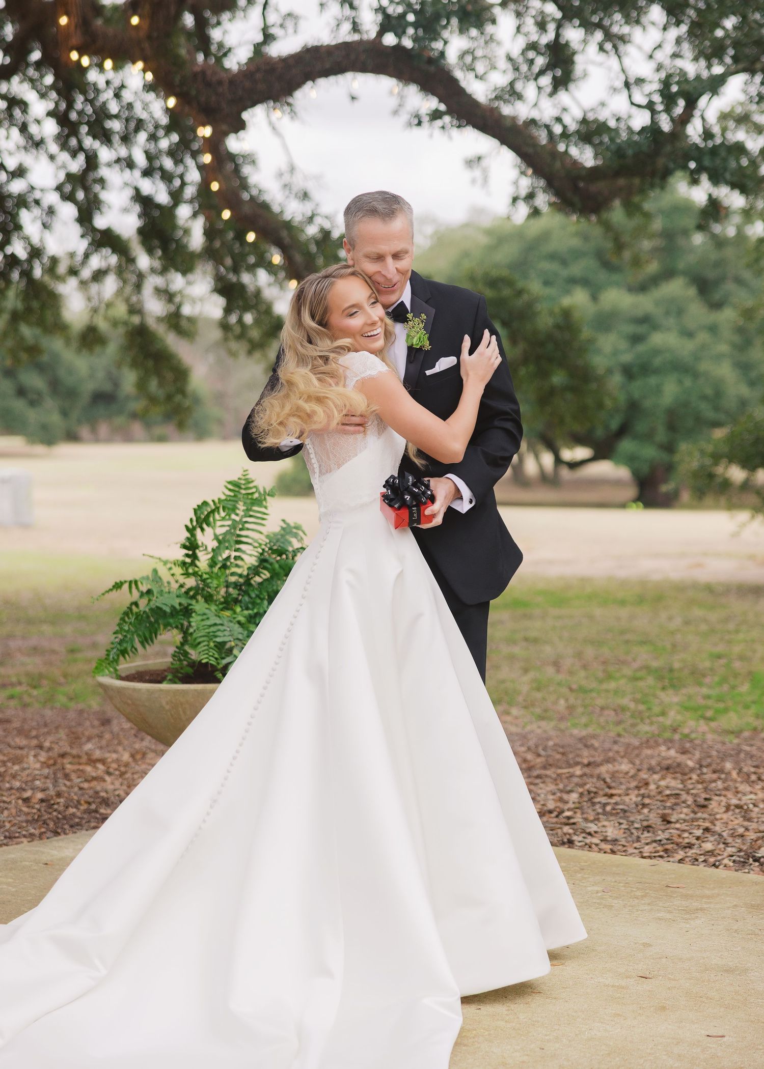 A couple in formal wedding attire shares a romantic kiss under a tree during their outdoor wedding photoshoot.