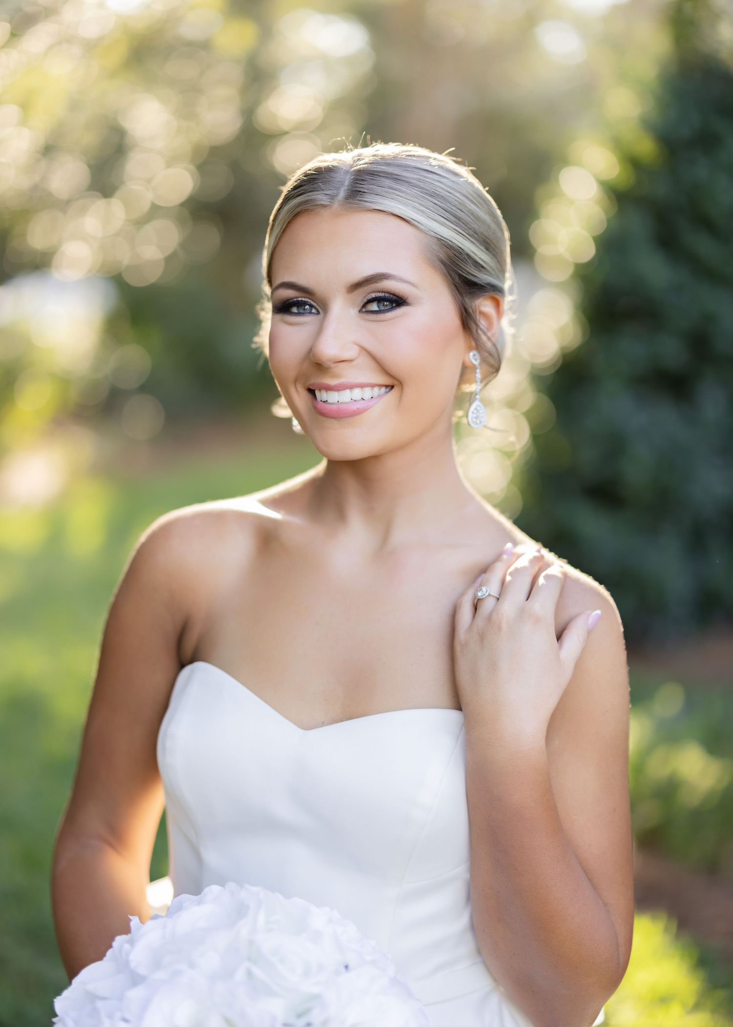 A bride in a strapless white wedding gown poses outdoors with a natural bokeh background in multiple shots.