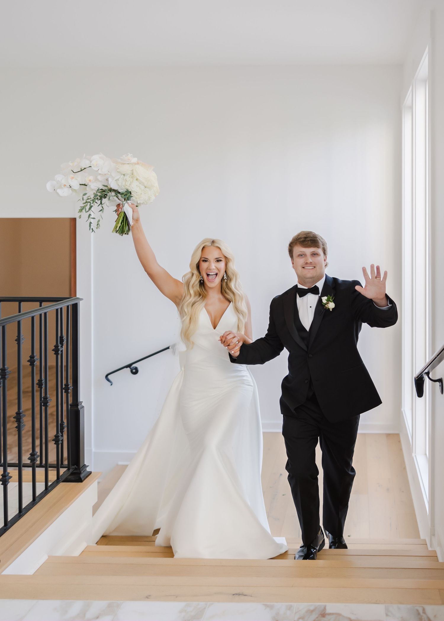 Joyful wedding couple walking and celebrating in bright white hallway.