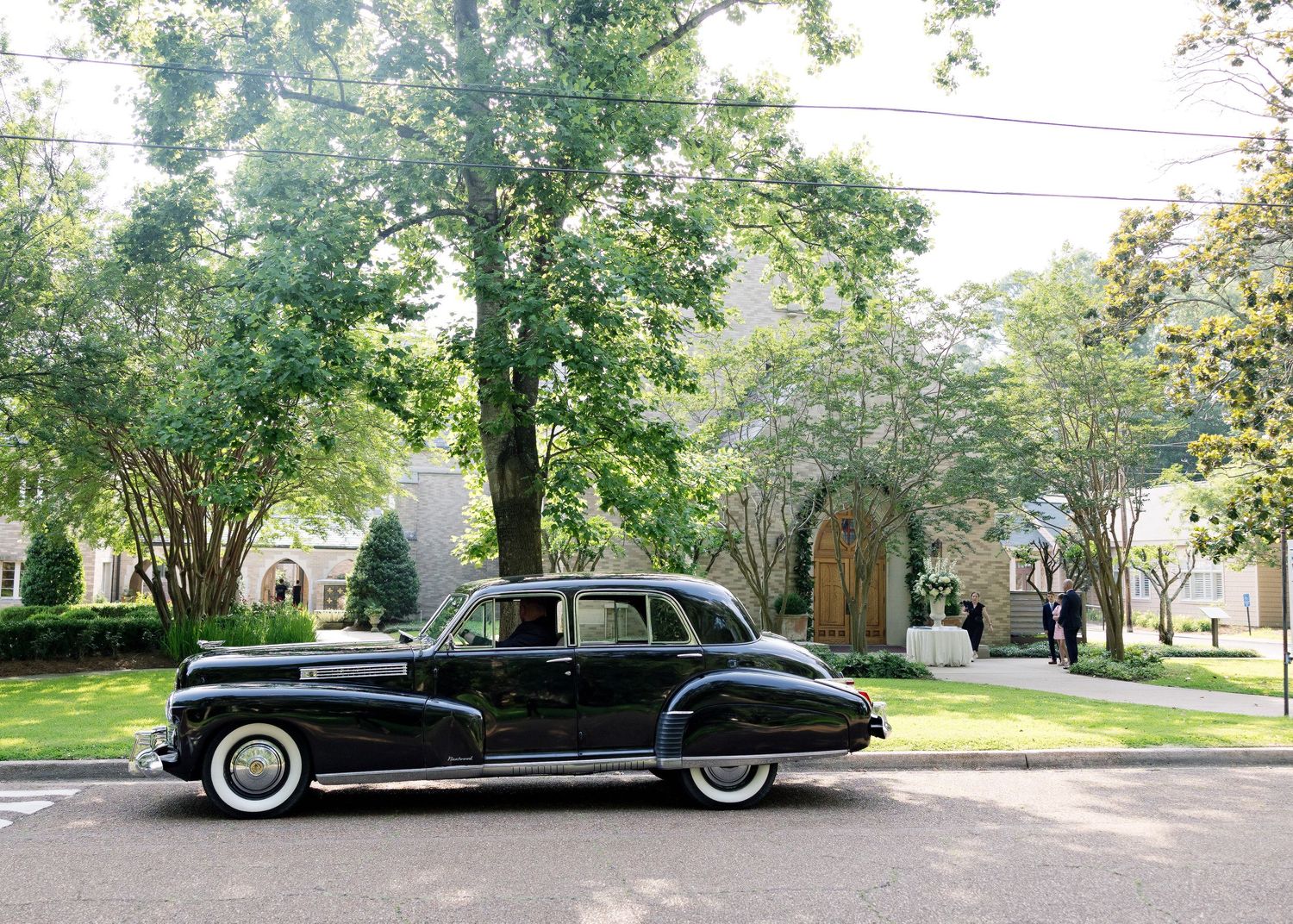 Vintage black Cadillac parked on a tree-lined residential street.