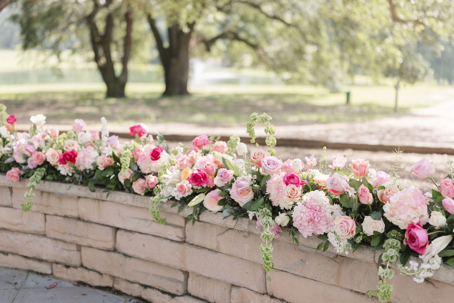 Pink and white floral arrangements decorating a stone wall at an outdoor wedding venue.