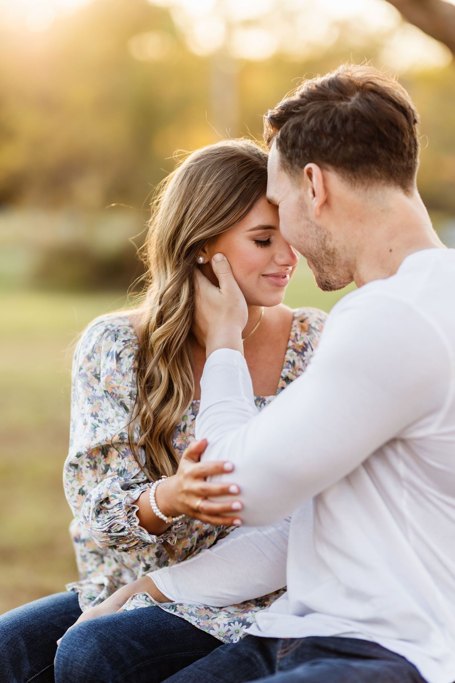 Romantic couple embraces during golden hour engagement photoshoot in a floral dress and white shirt.