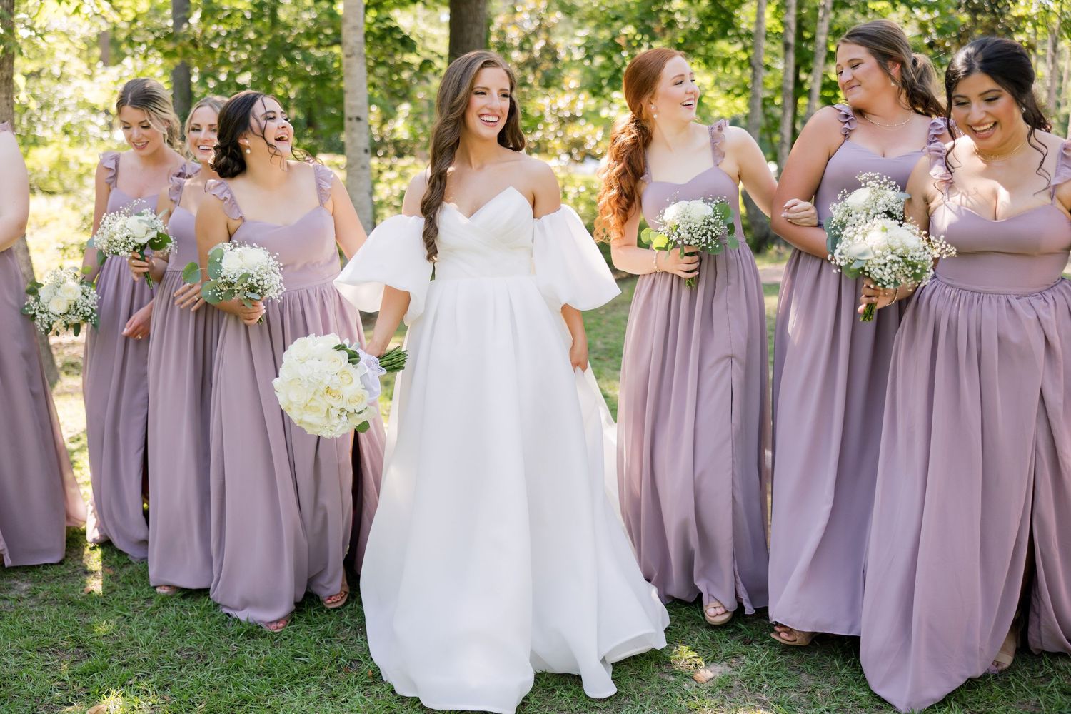 Bridal party in lavender dresses with white bouquets outdoors.