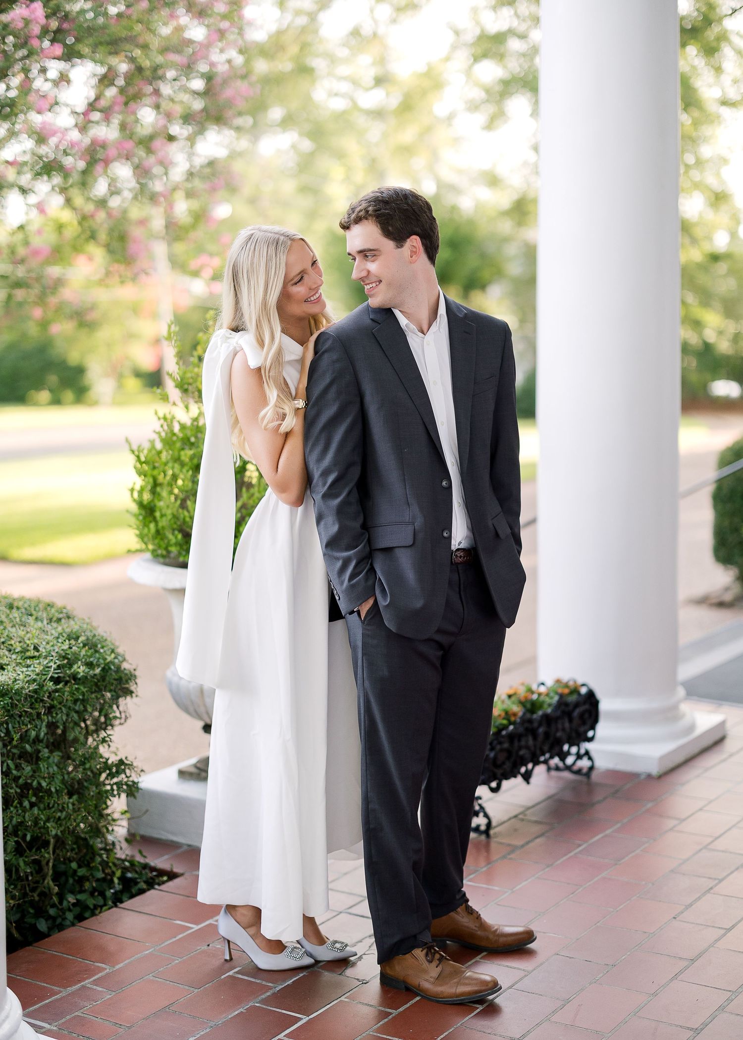 Elegant scene on brick porch with white columns and flowering garden.