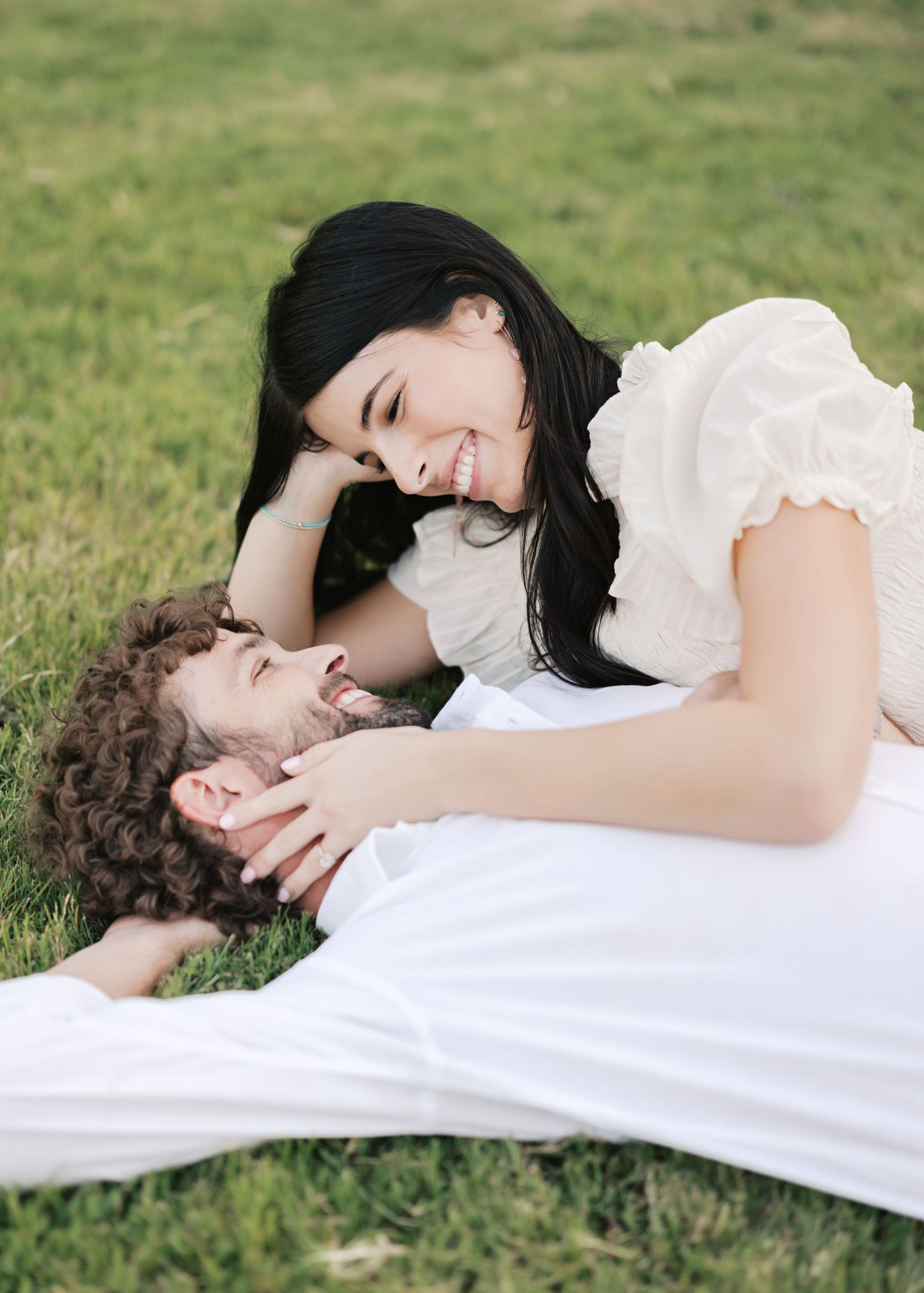 A couple laying on grass sharing a tender moment while smiling at each other.