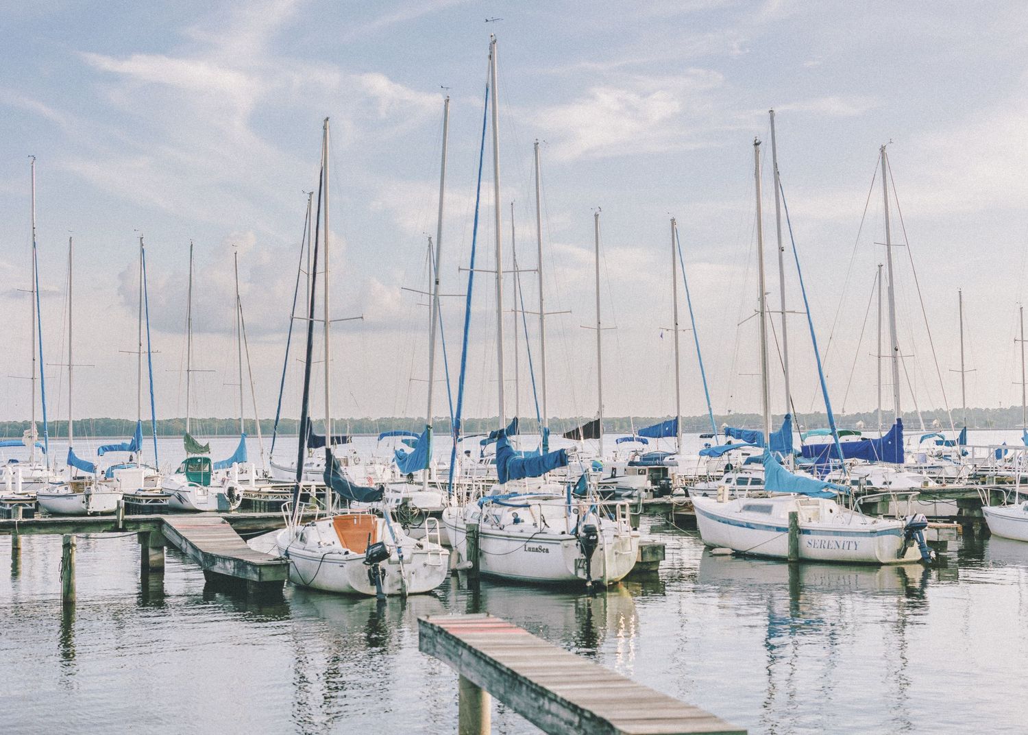 Boats docked in rows at a marina with calm waters and cloudy skies creating a serene nautical scene.