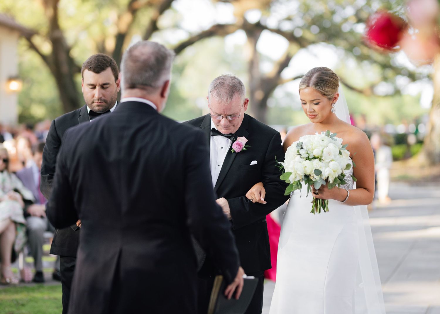 Wedding ceremony setup outdoors with elegant white floral arrangements and guests in formal attire.