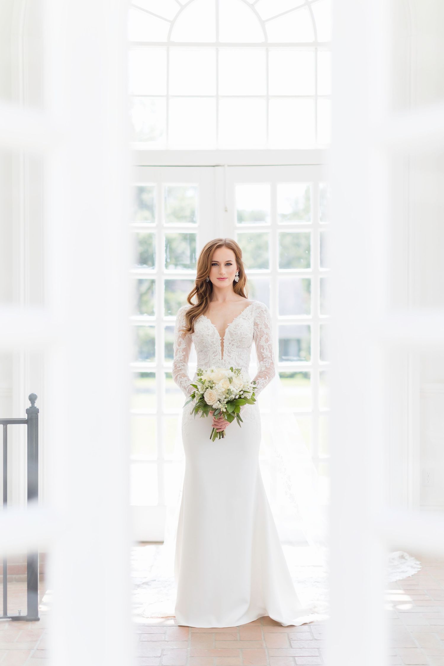 Ethereal bridal portrait in a bright white room with large windows and classic bouquet.