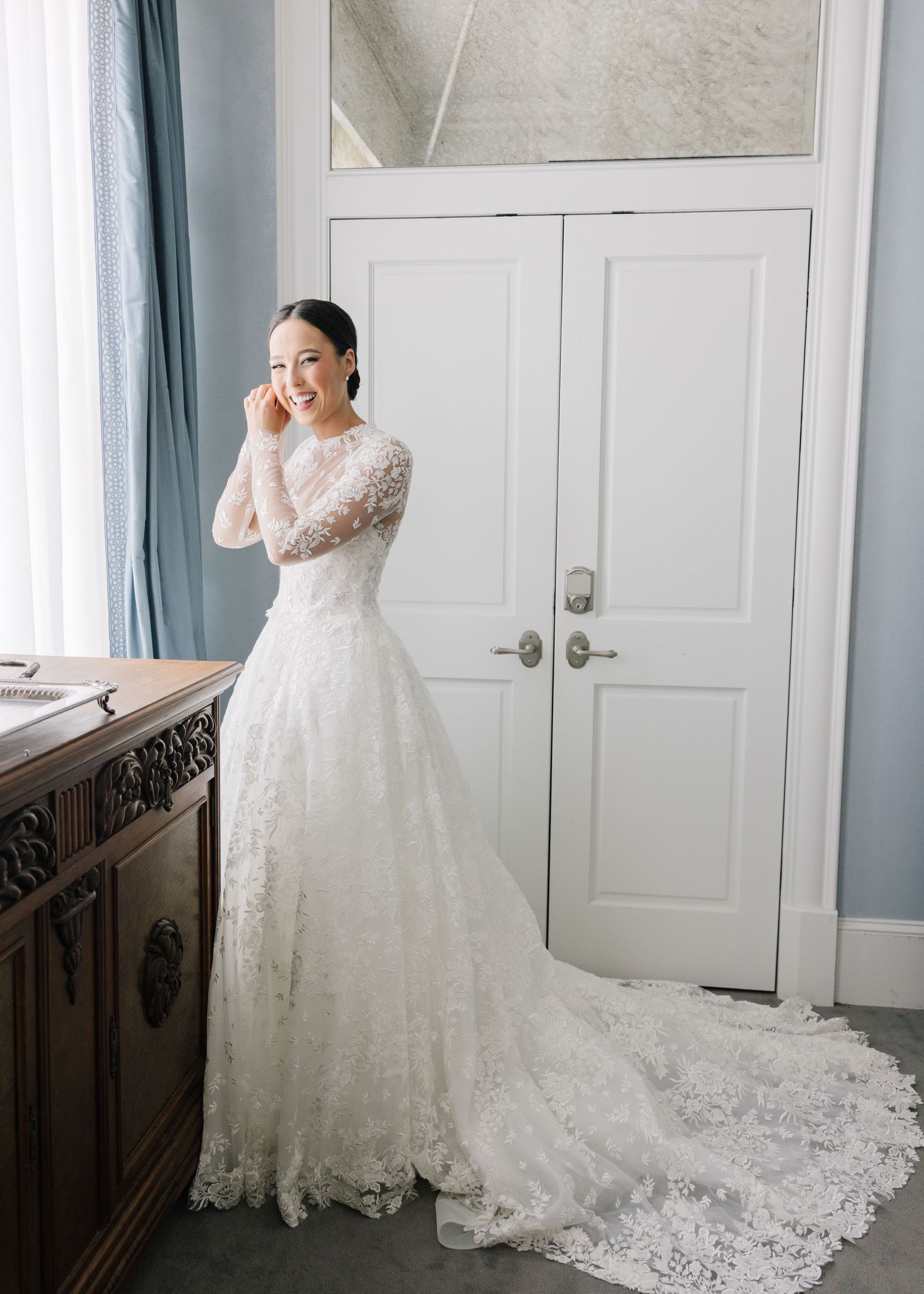 Romantic full-length lace wedding gown with long train photographed in natural light.