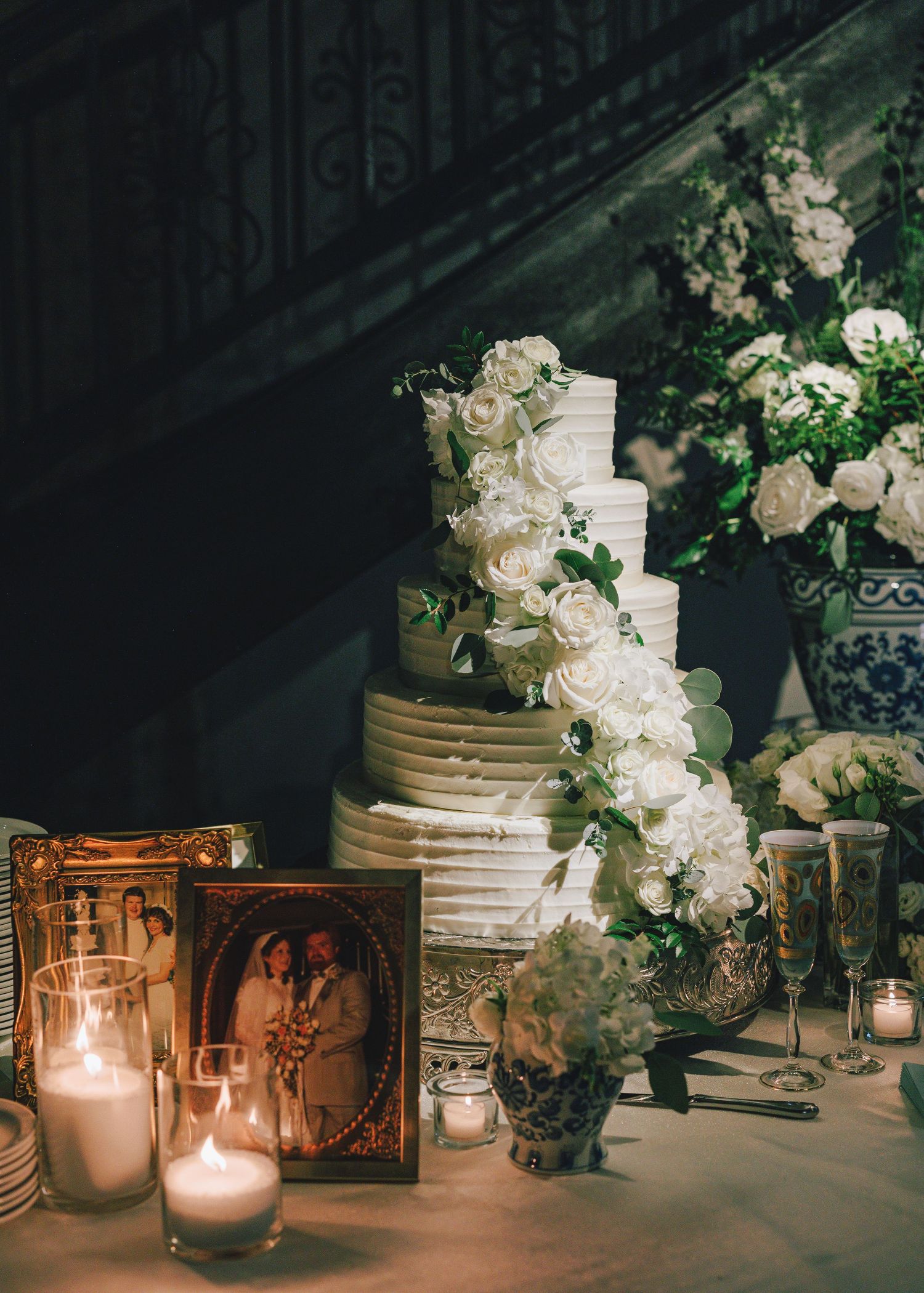 Elegant wedding cake display with white orchids, glowing candles, and vintage frames creating a romantic atmosphere.