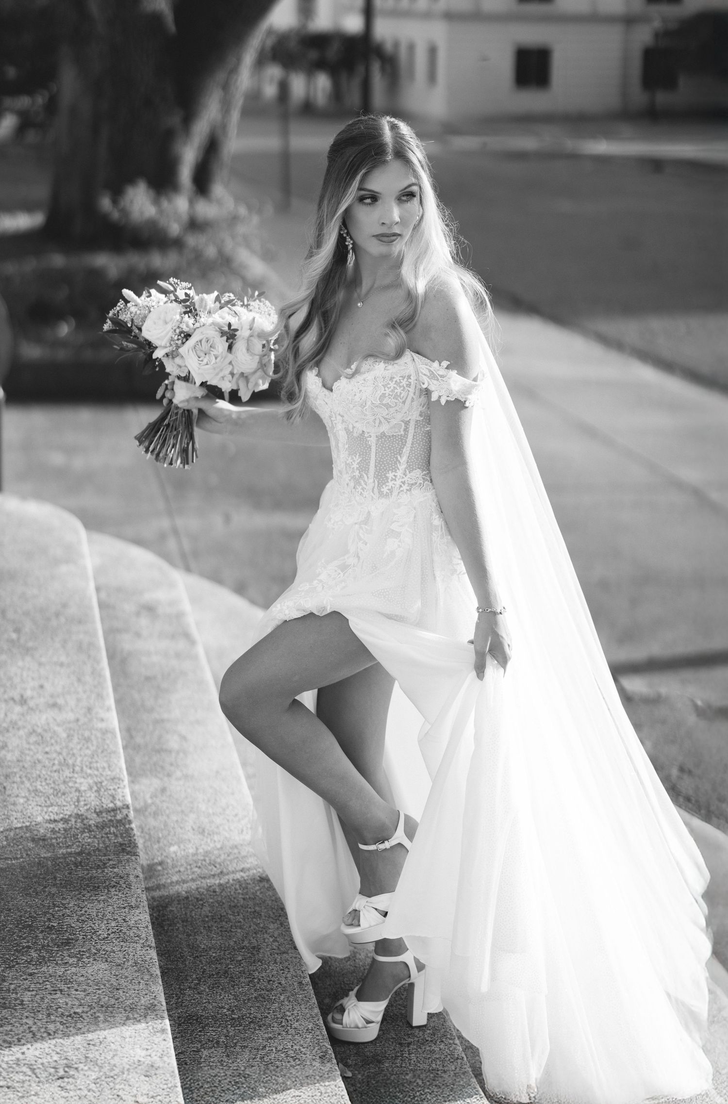 Black and white photo series showing a bride in a flowing white dress and garter adjusting her stockings outdoors.