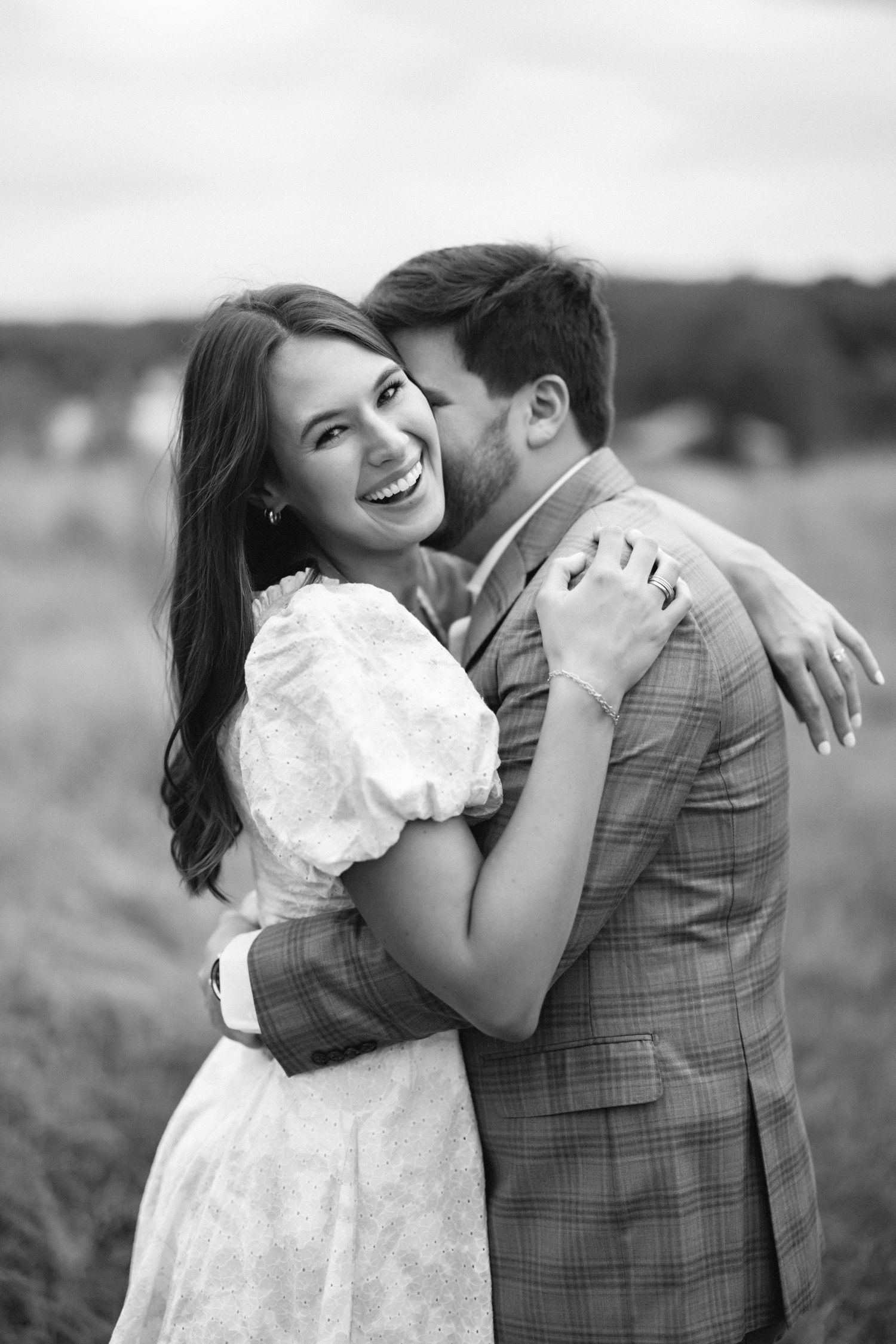 A romantic black and white portrait of a couple embracing in an outdoor field.