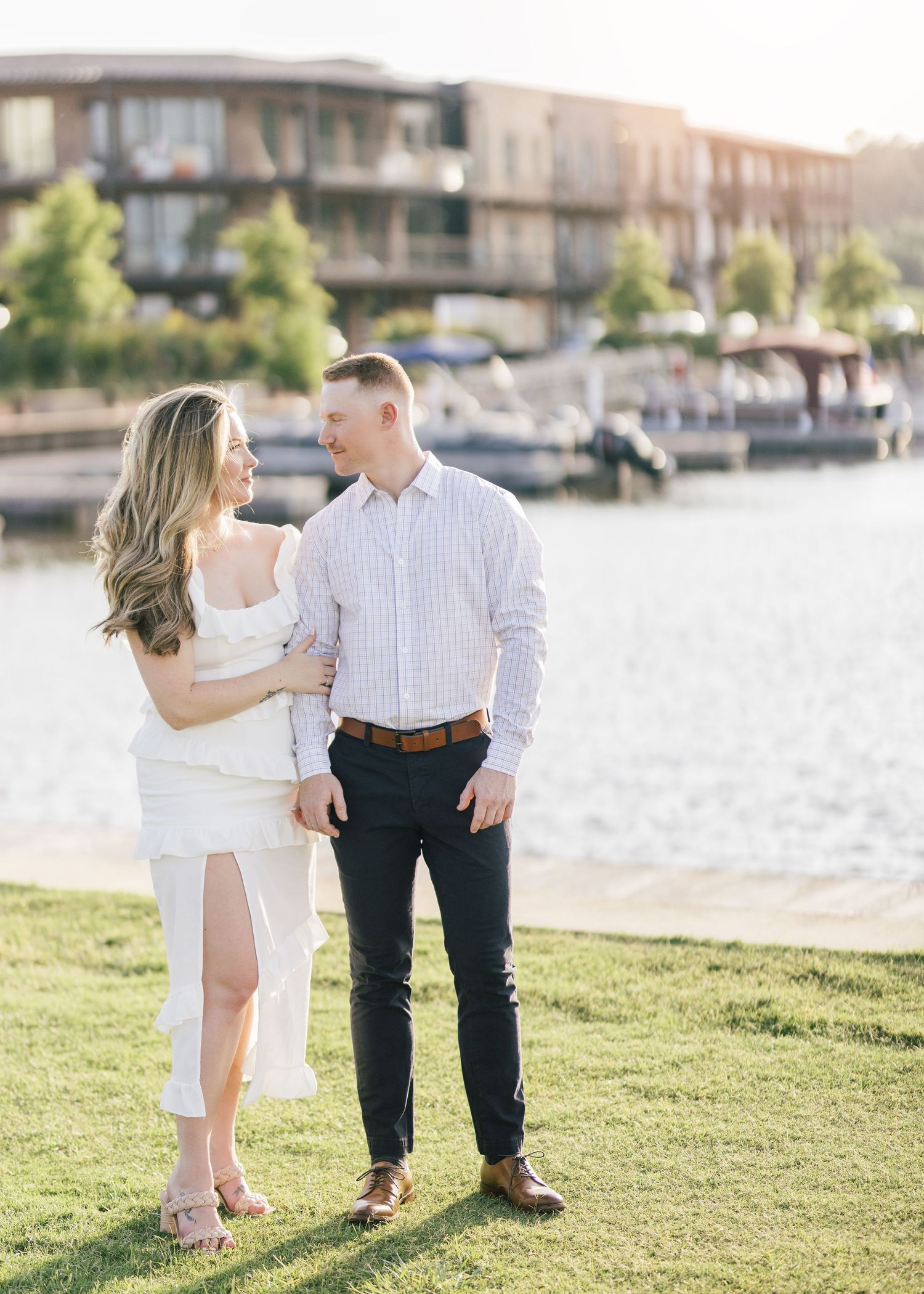 Couple enjoying playful moments together on grassy waterfront area.