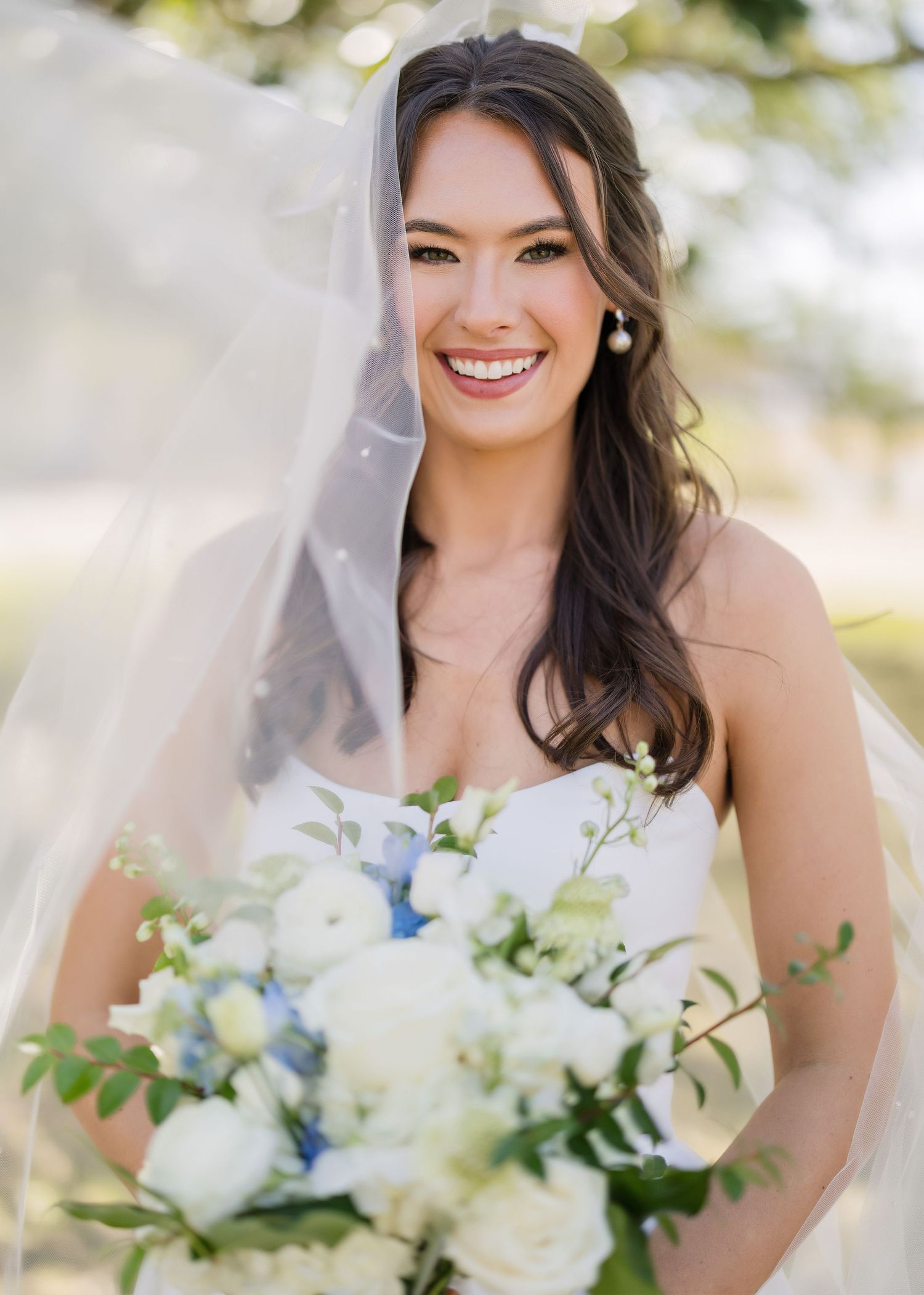 Wedding portraits featuring a bouquet with white and blue flowers against an outdoor backdrop.