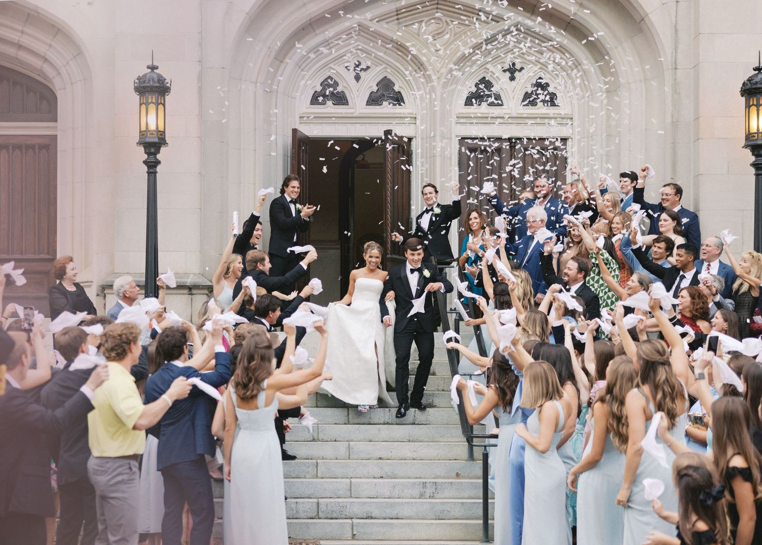 Wedding guests shower newlyweds with confetti as they exit church steps.