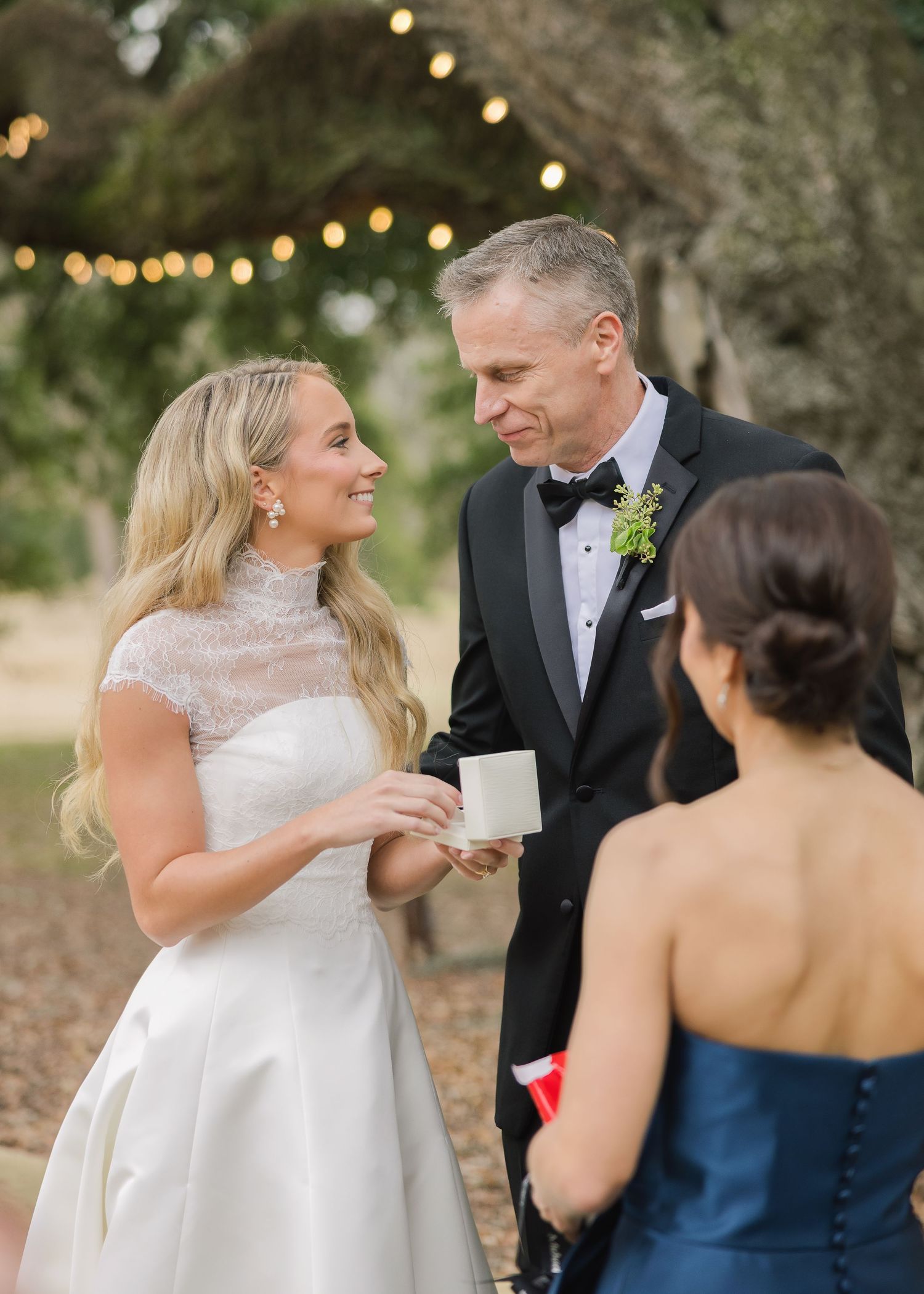 Wedding guests share laughter and conversation during an outdoor evening reception with twinkling lights in the background.