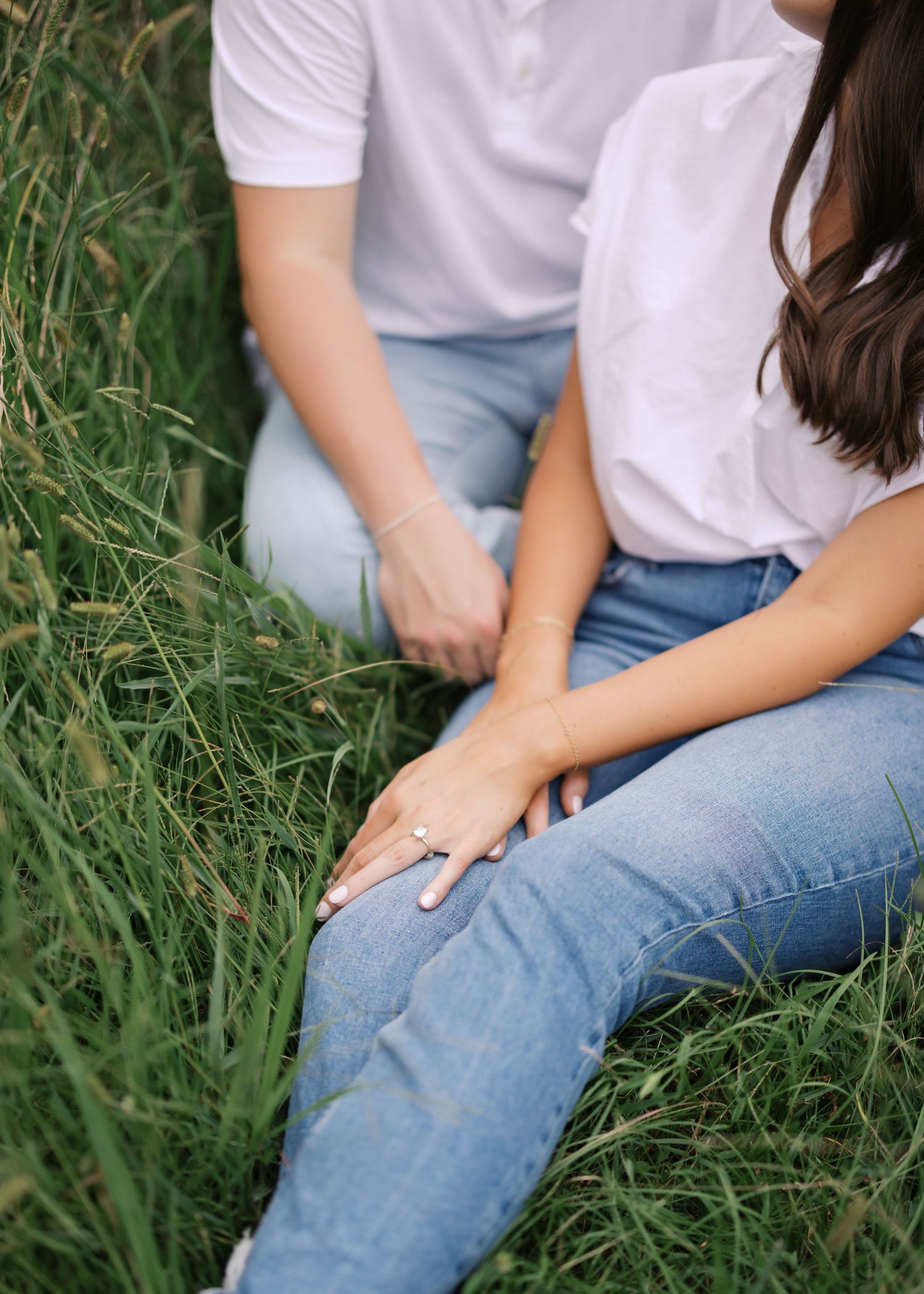 Close-up of hands wearing an engagement ring while sitting in tall grass.