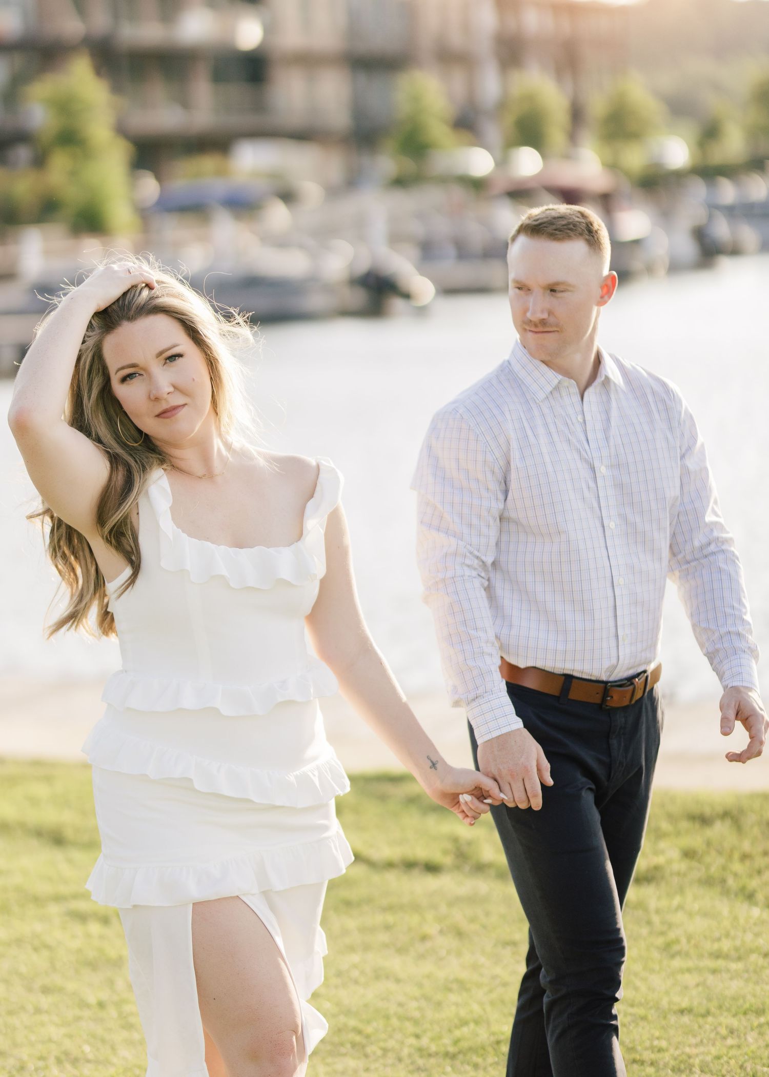 Couple in coordinated white outfits dancing together on grass near a waterfront.