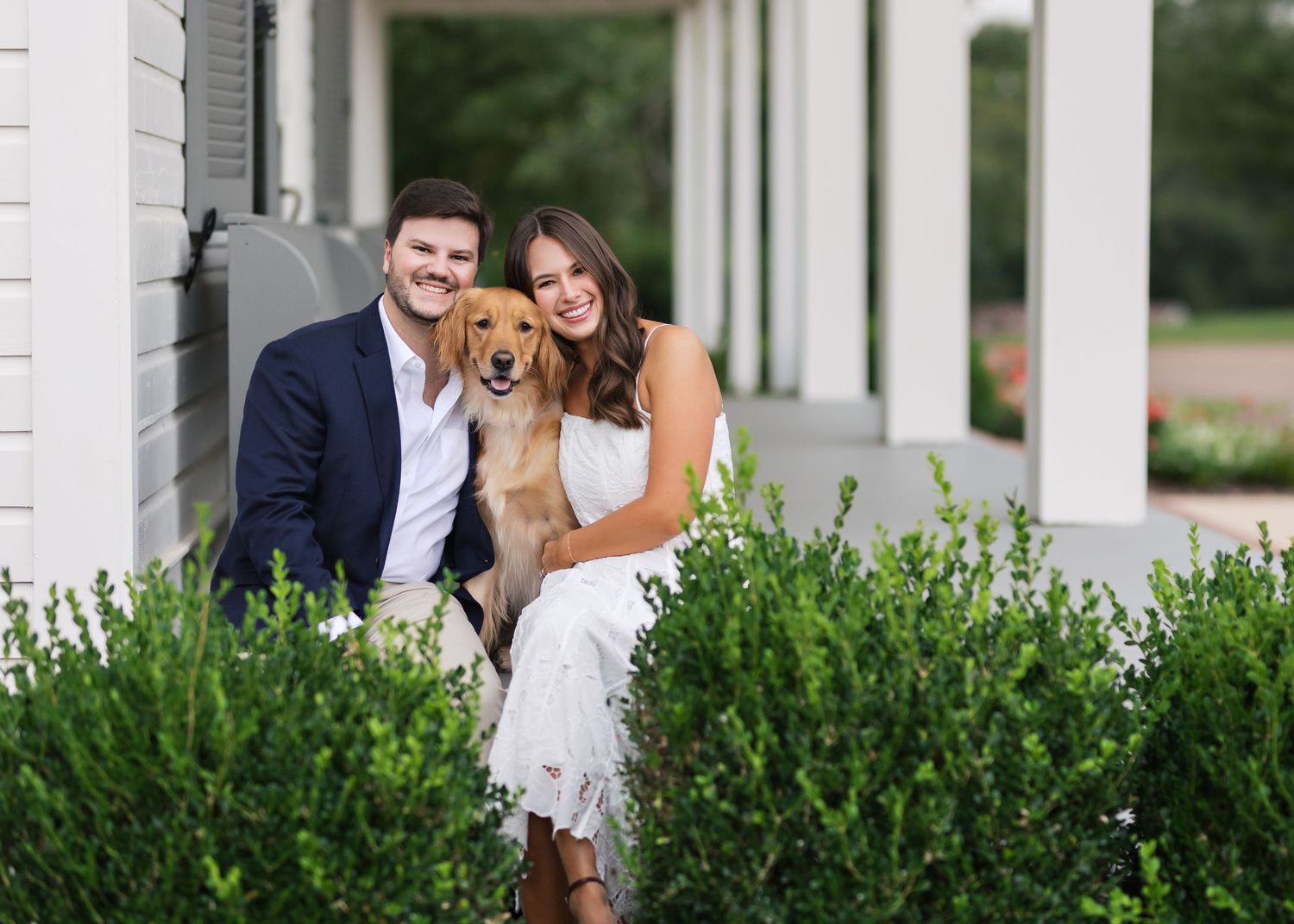 Couple poses with their golden retriever in front of white pillared building.