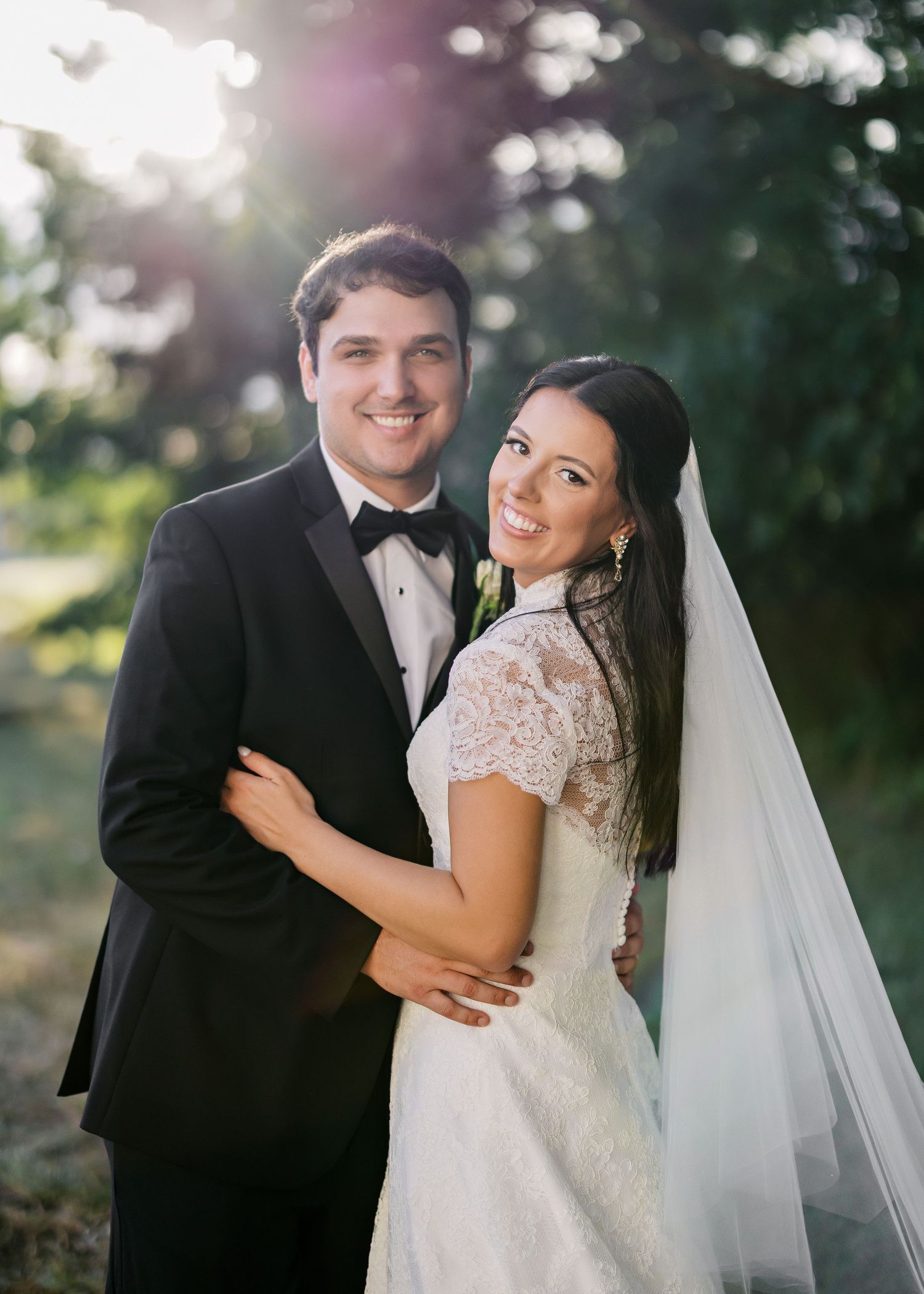 Wedding couple poses together outdoors in a garden setting with soft natural lighting.