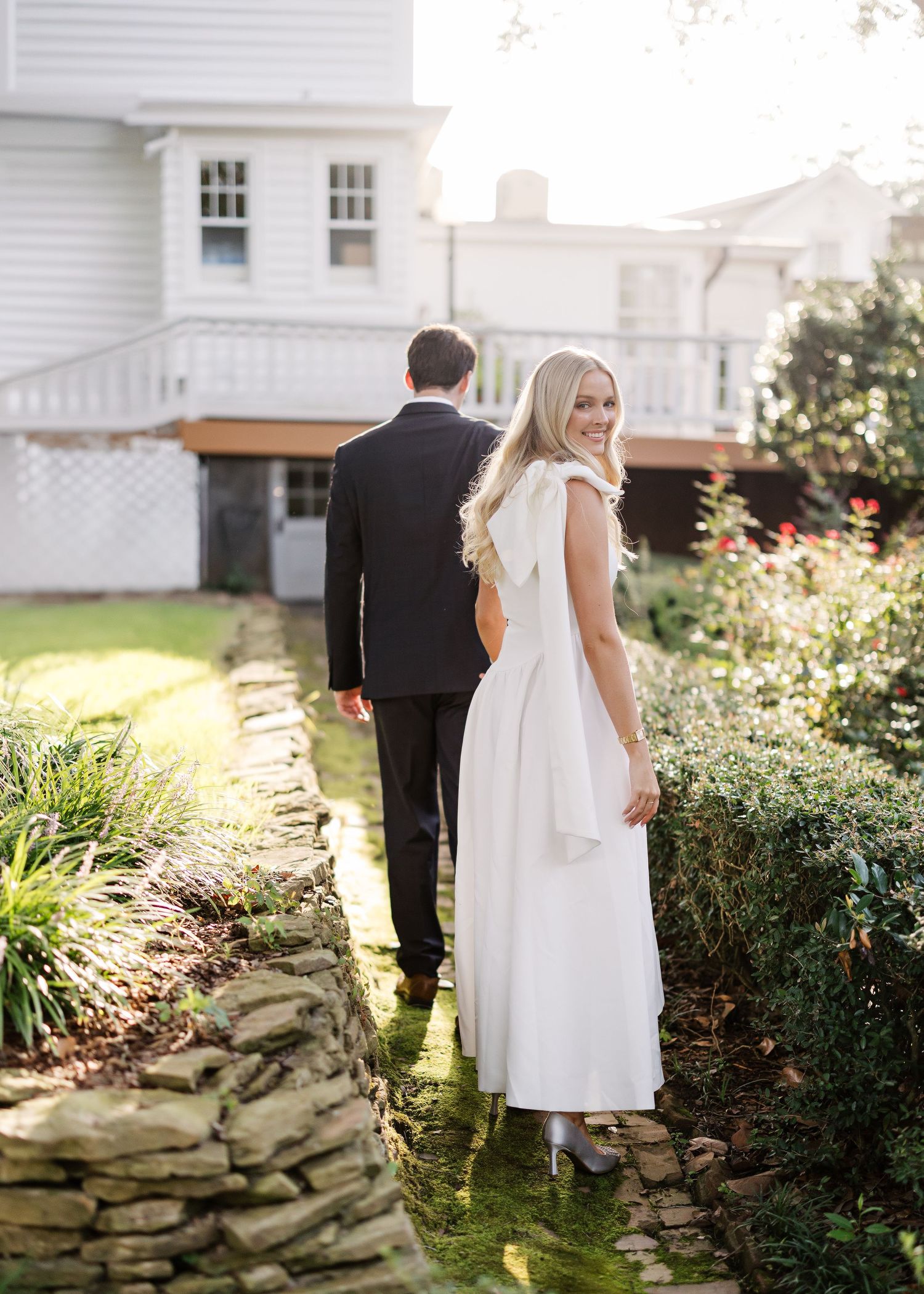 Garden scene with white dress against classic white colonial architecture and stone wall.