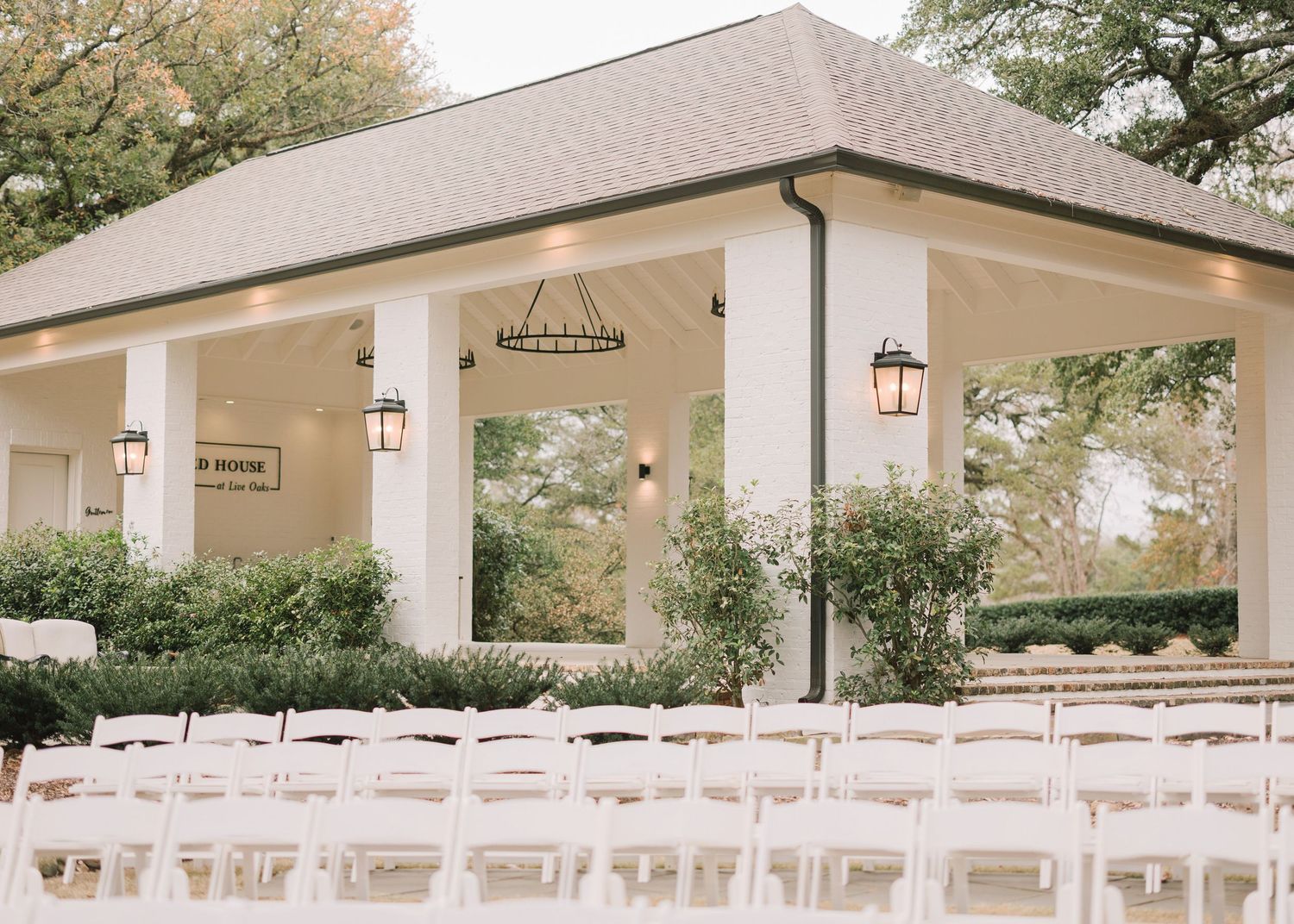 Long view of an elegant white wedding venue with covered patio and outdoor ceremony seating.