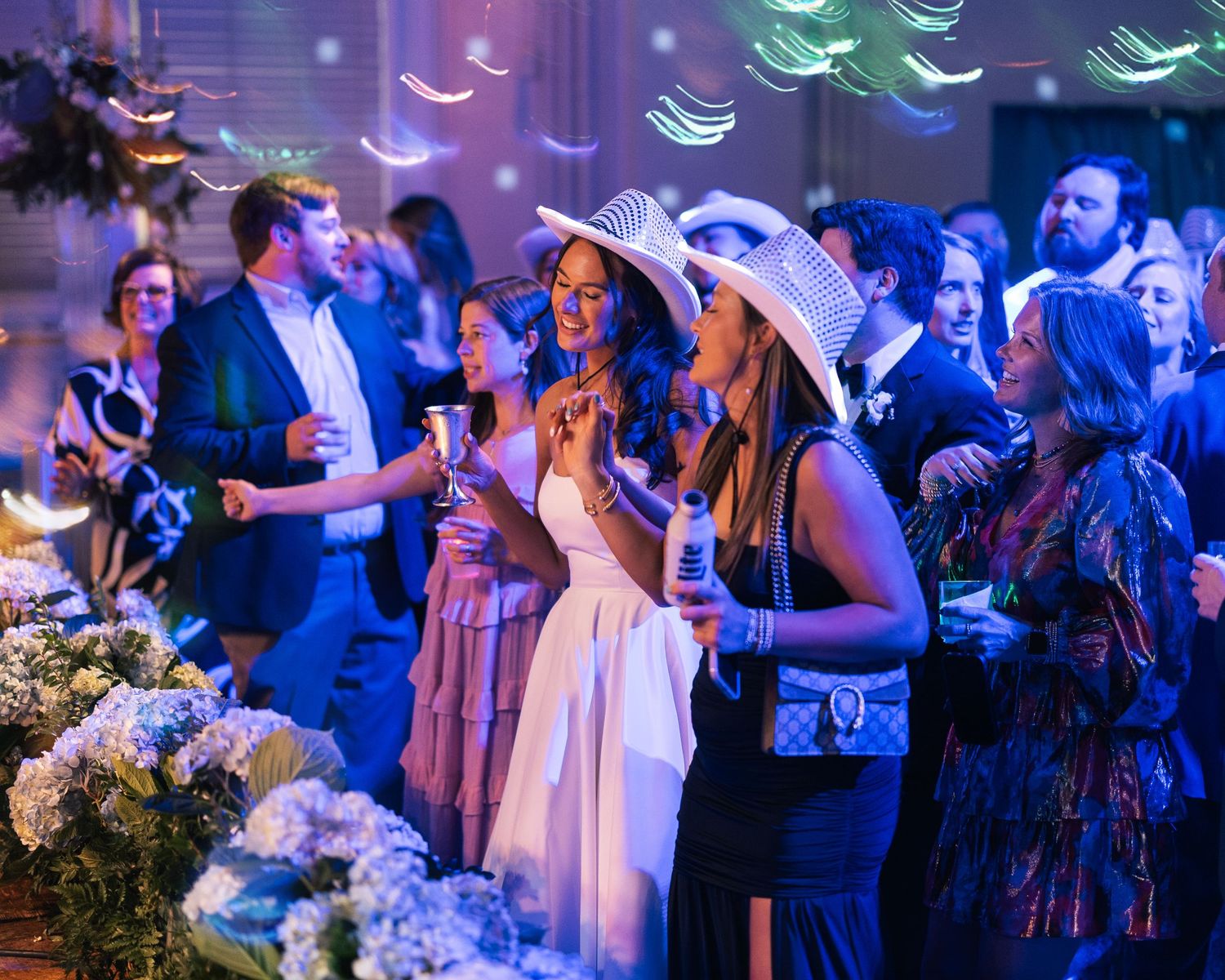 Wedding guests dance and celebrate on a dance floor illuminated by blue lighting during an evening reception.