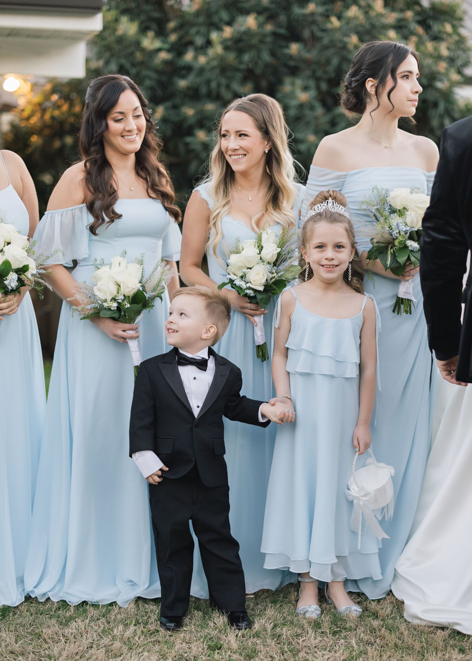 Wedding party with bridesmaids in powder blue dresses and young attendants in formal wear on grassy lawn.