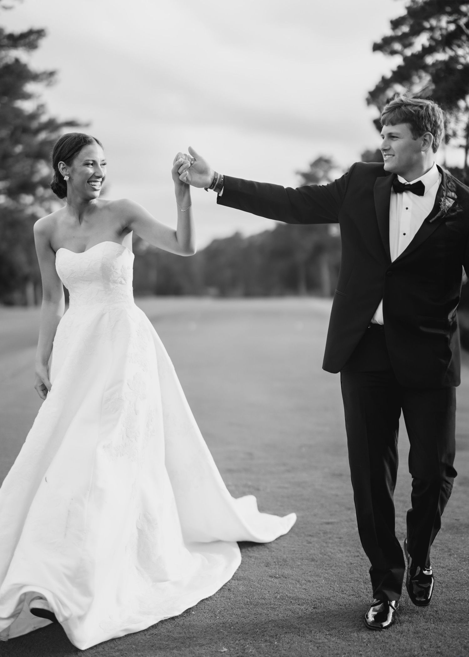 Elegant couple walks together across an open field in formal wedding attire.