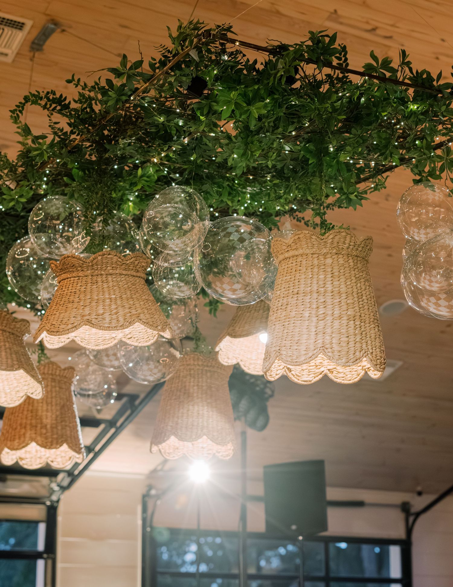 Woven basket lampshades hang from a wooden ceiling with green foliage decorations creating a natural ambiance.