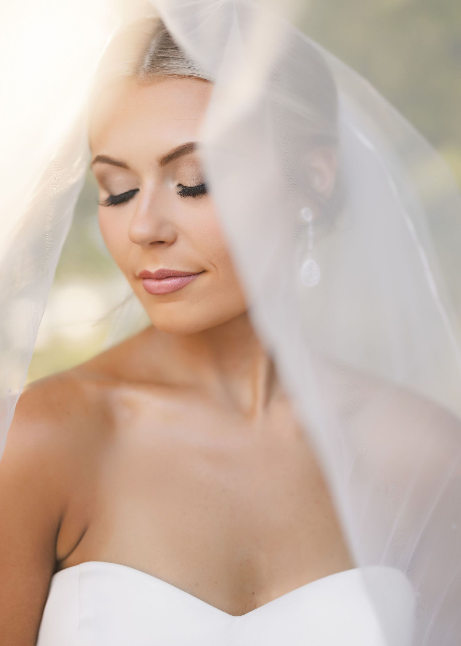 Ethereal bridal portrait with delicate white veil and strapless gown captured in soft, dreamy lighting.