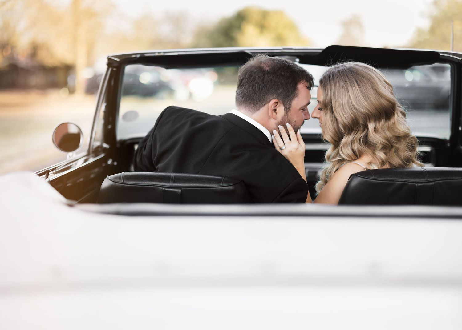 Newlyweds share intimate moments while sitting in vintage car.