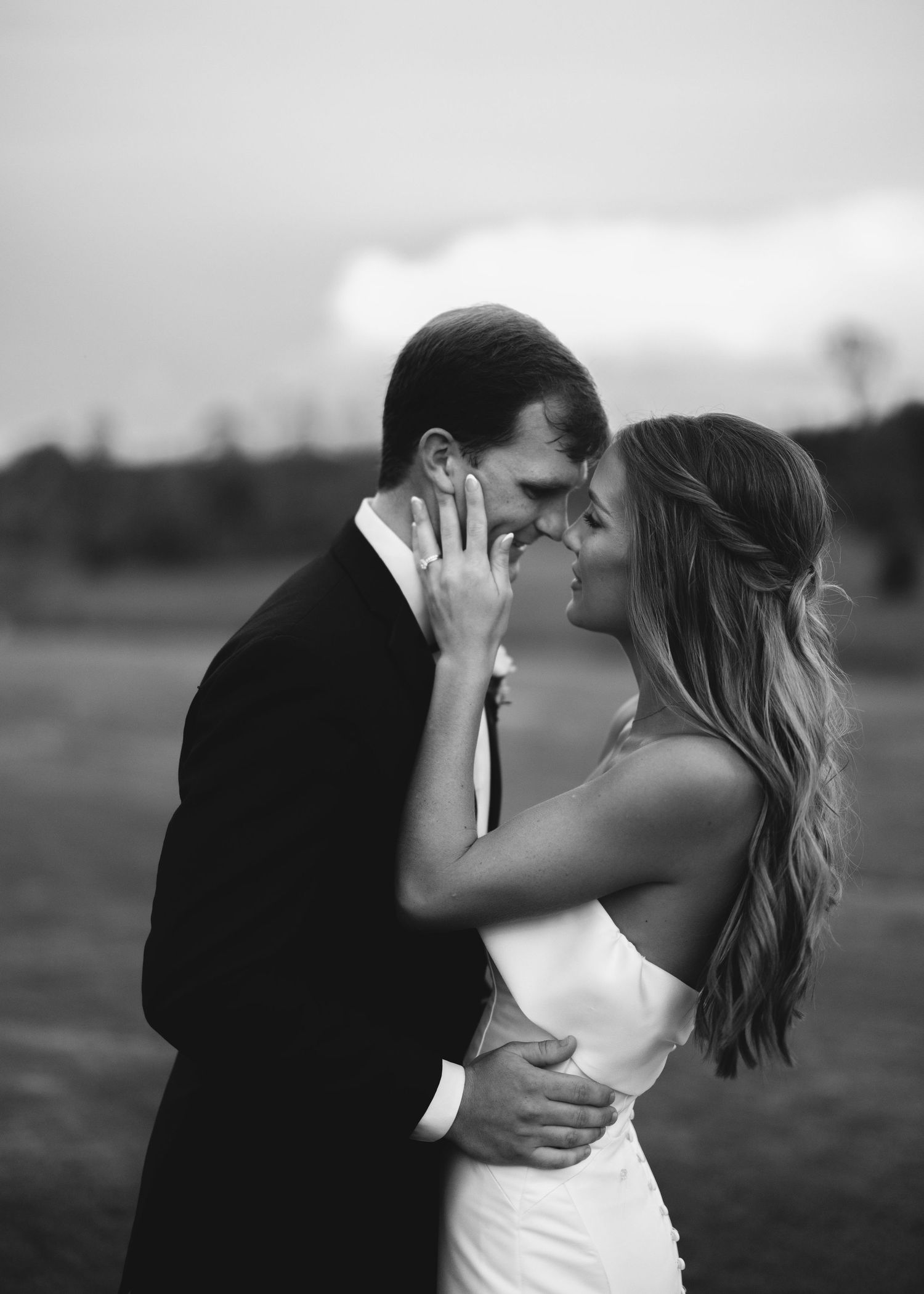 A romantic black and white photo series showing a couple embracing and kissing in an outdoor field at sunset.