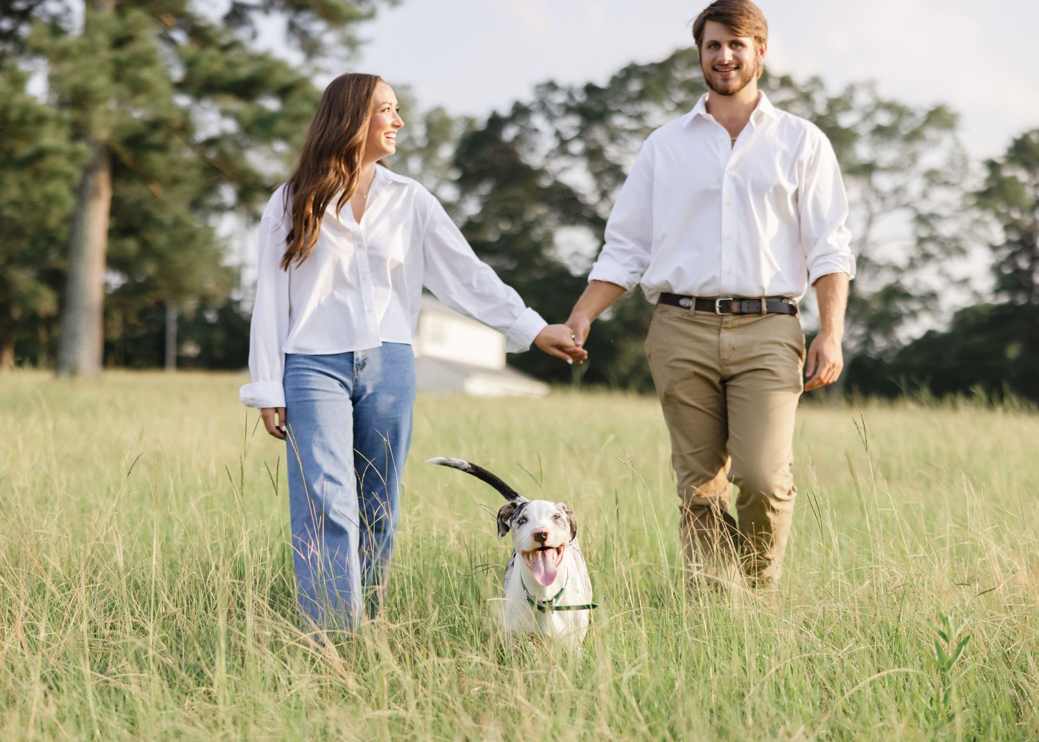 Couple walking dog in sunny field wearing casual white and khaki outfits.