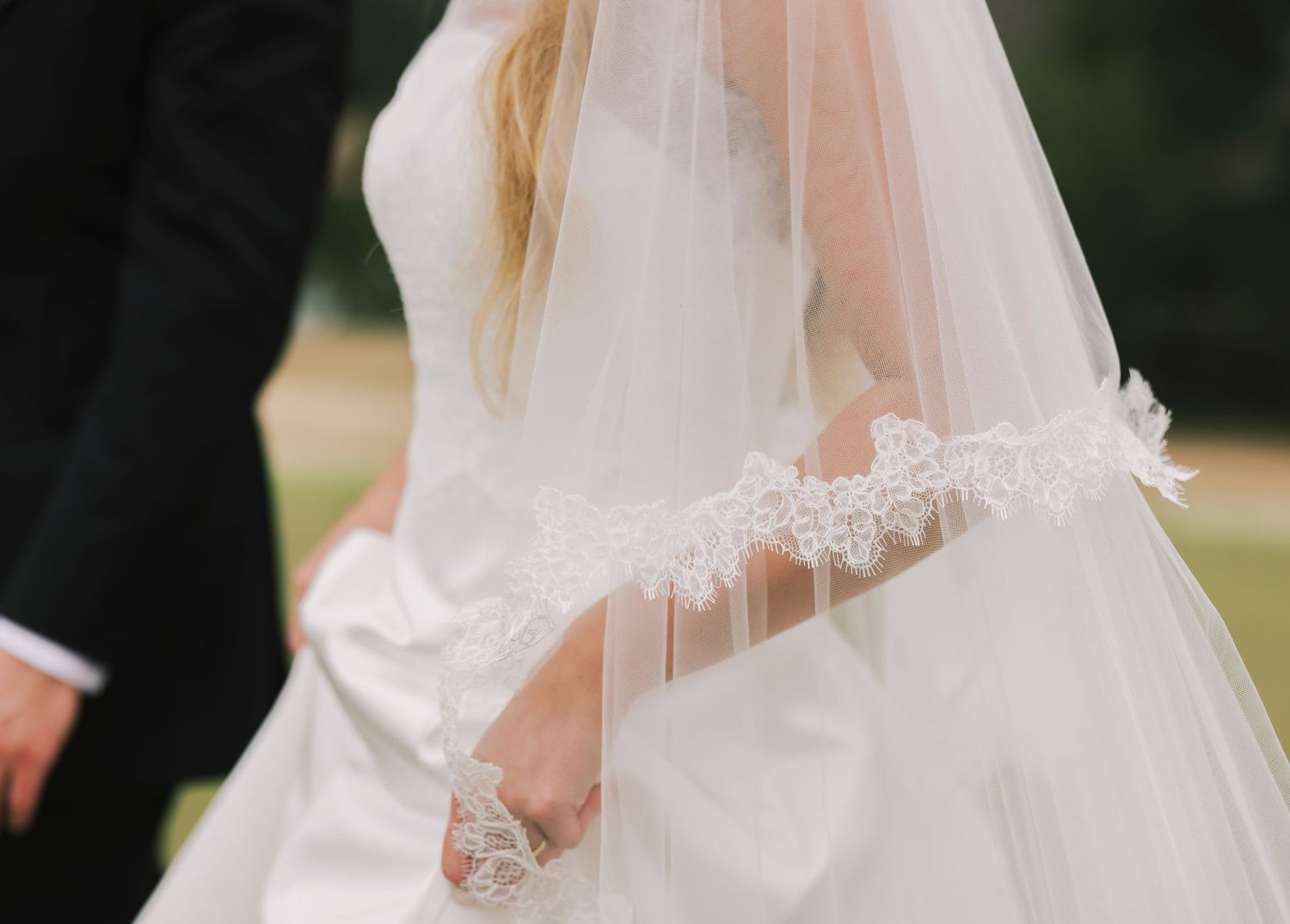 A bride in a white wedding dress and veil walks through a garden setting during a wedding ceremony.