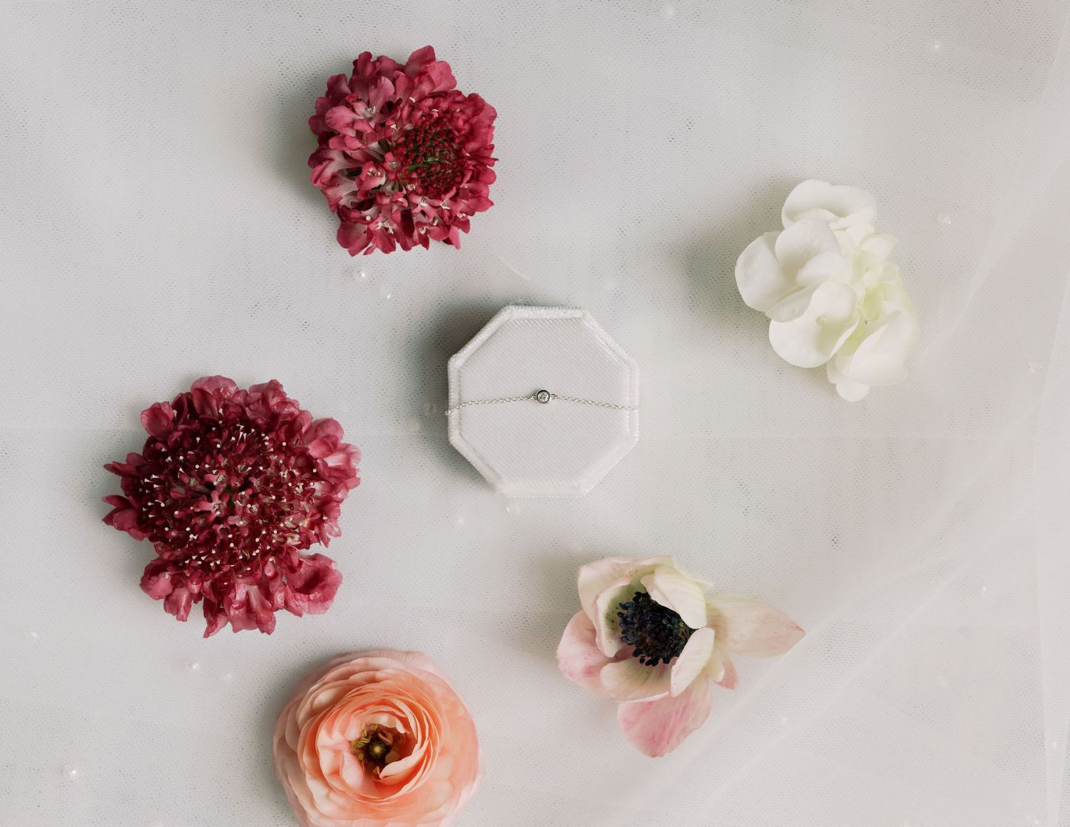 Delicate ring box surrounded by pink and white flowers on light background.