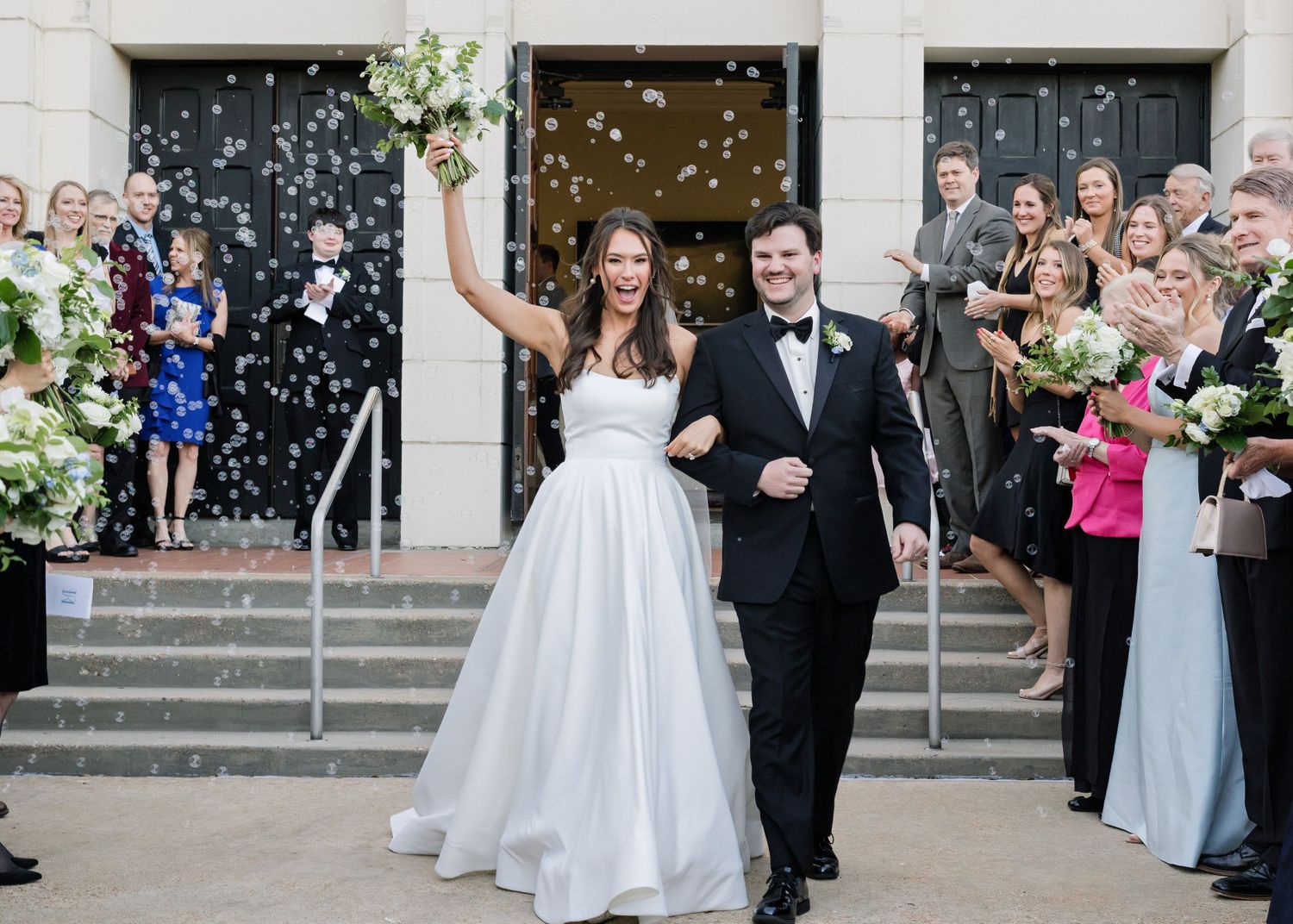 Newlyweds exit church steps while guests shower them with confetti on their wedding day celebration.