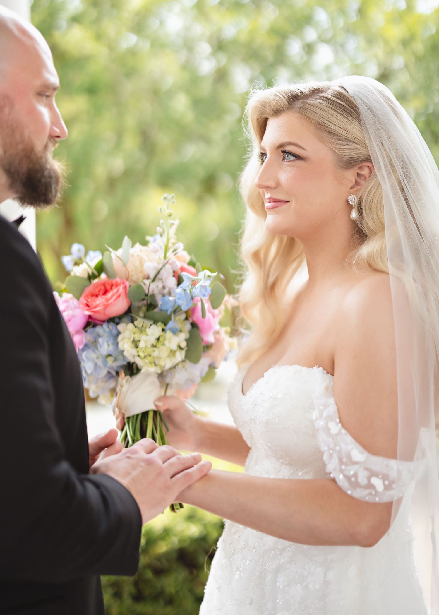 Romantic outdoor wedding ceremony moment with couple exchanging vows among spring flowers.