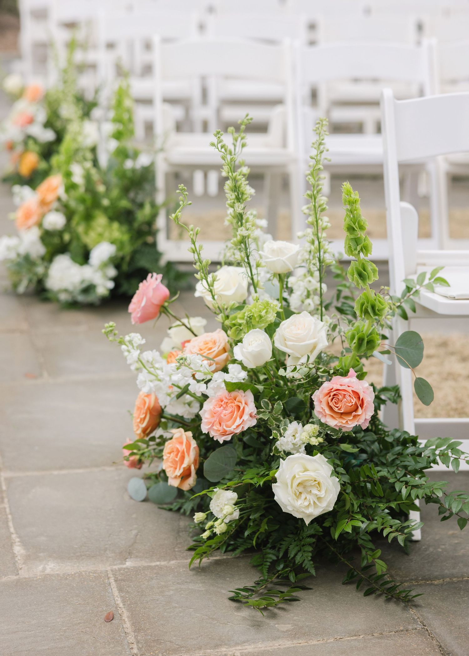 Elegant wedding ceremony floral arrangements with peach roses and white flowers adorning stone steps outdoors.