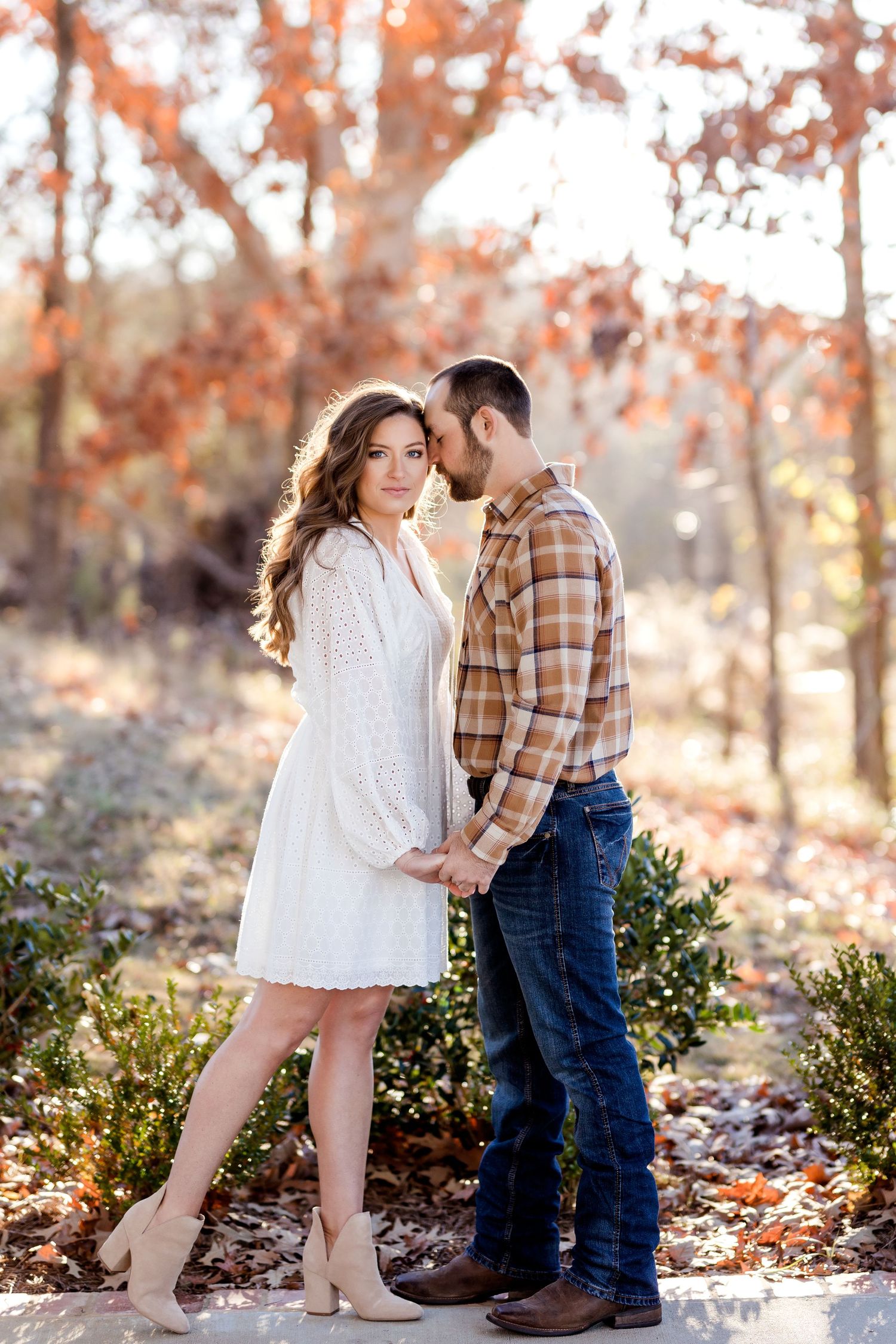 Couple in casual outfits sharing romantic moments among autumn leaves.