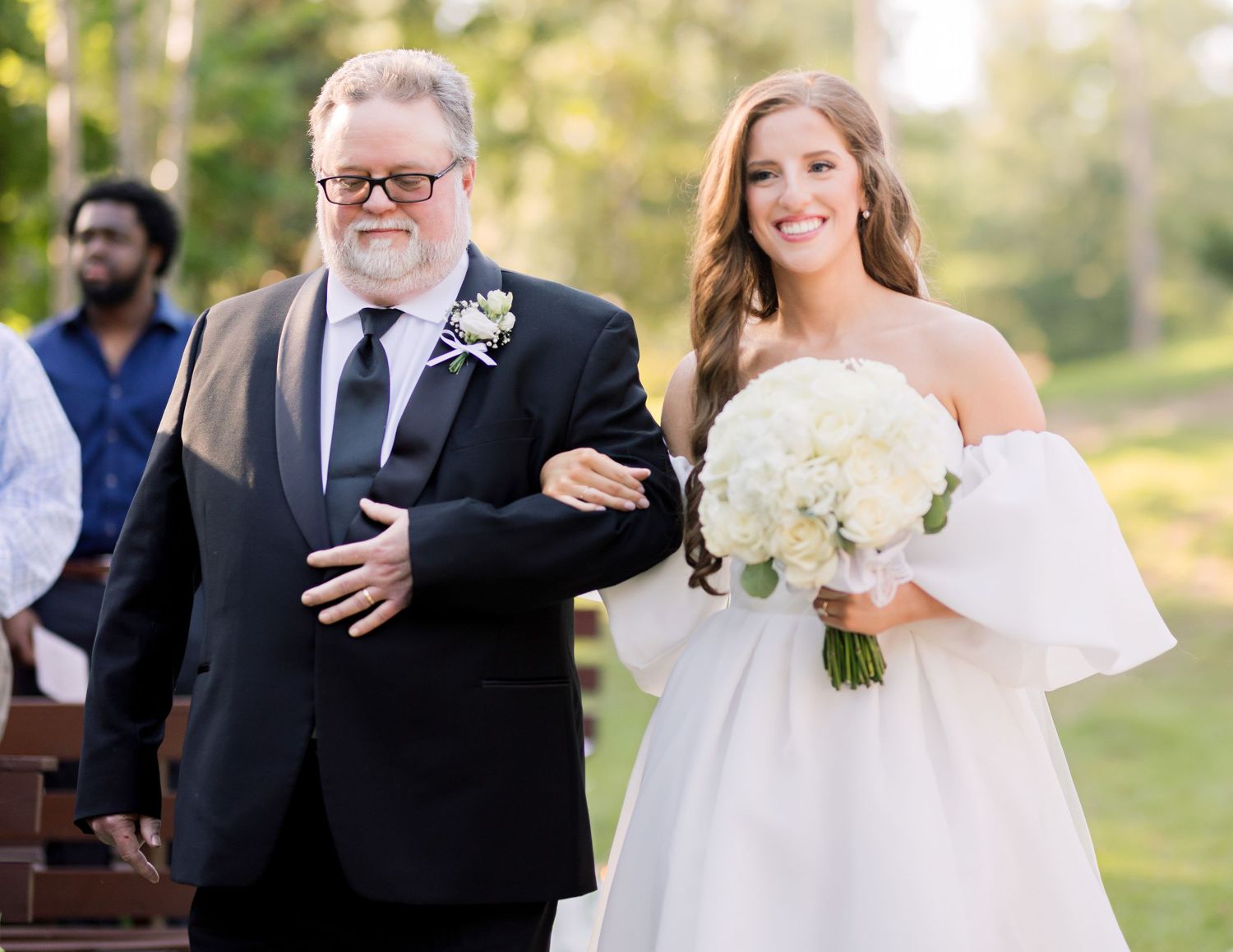 Wedding processional moment captured outdoors with white bouquet.