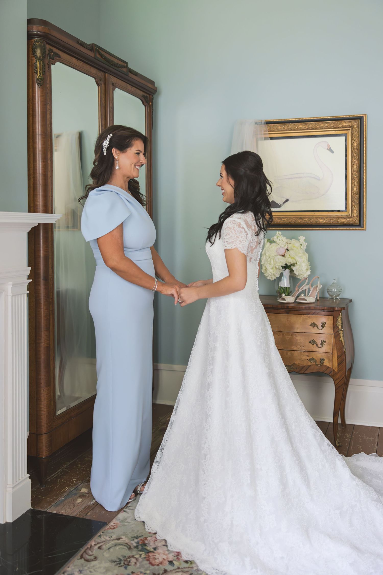 Intimate pre-wedding moment between bride in white gown and attendant in light blue dress.