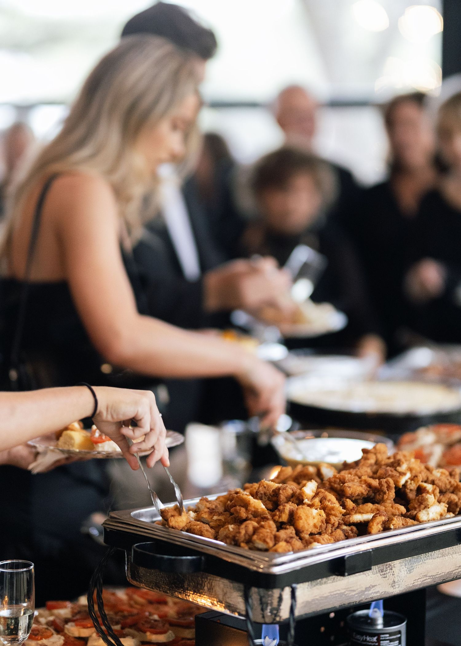 Wedding guests serving themselves from a buffet line with chafing dishes of appetizers.