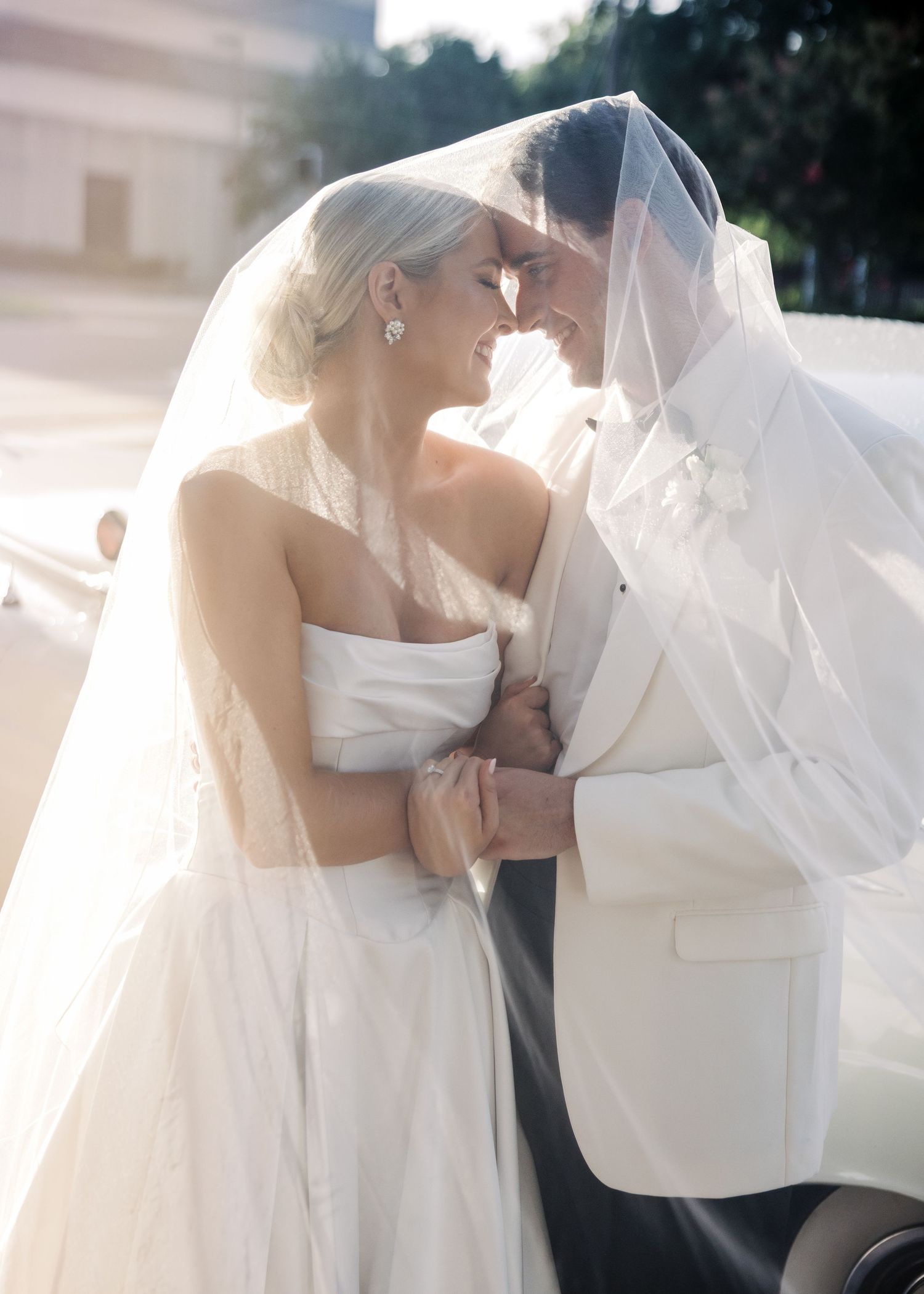 Romantic sunlit moment between newlyweds under bridal veil.